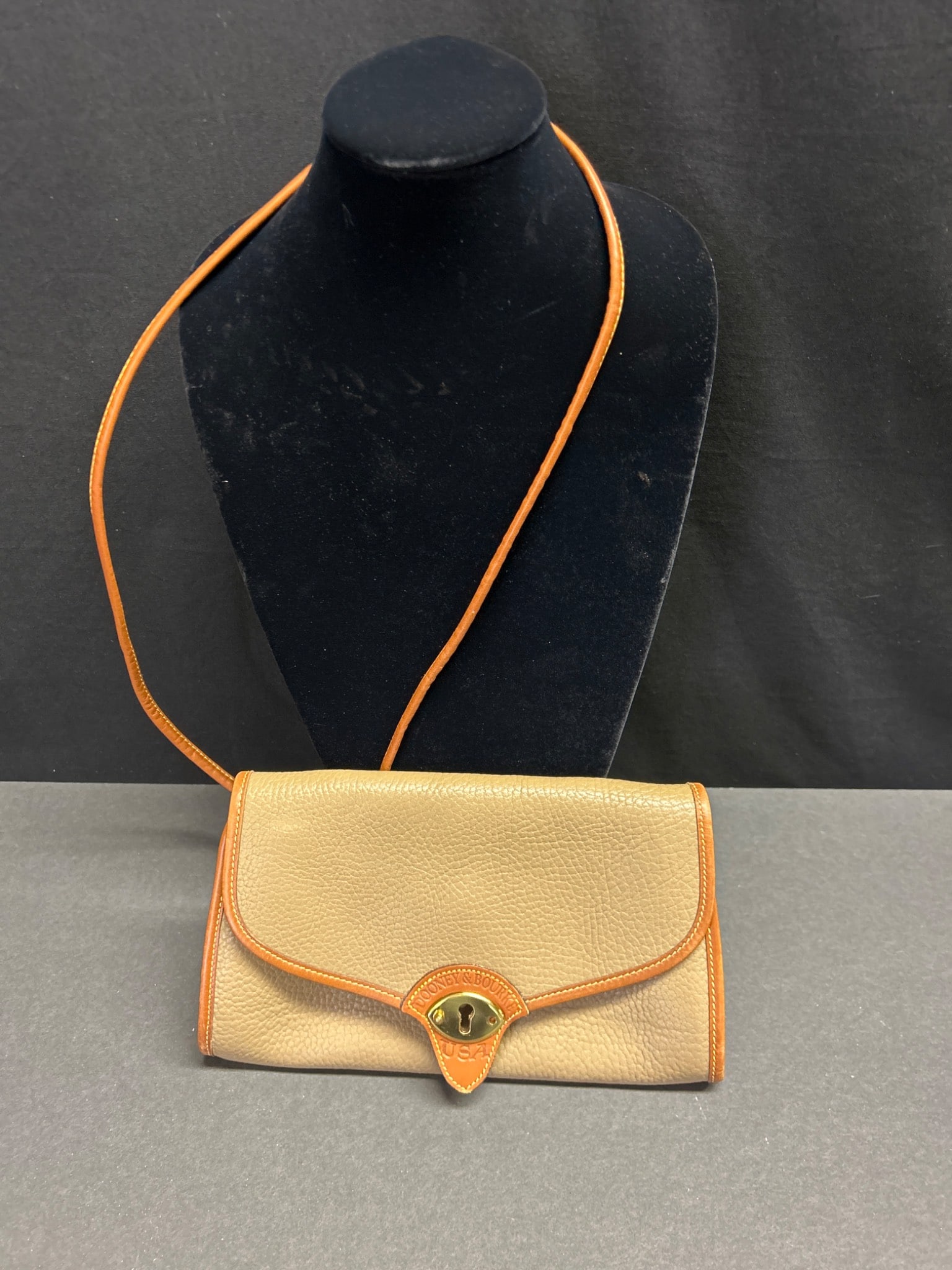 Dooney & Bourke USA Leather Crossbody Purse in Tan and Brown: This is a Dooney & Bourke leather crossbody purse, made in the USA. The bag features a tan textured leather body with brown leather trim and strap. The front flap has gold-tone hardware with a