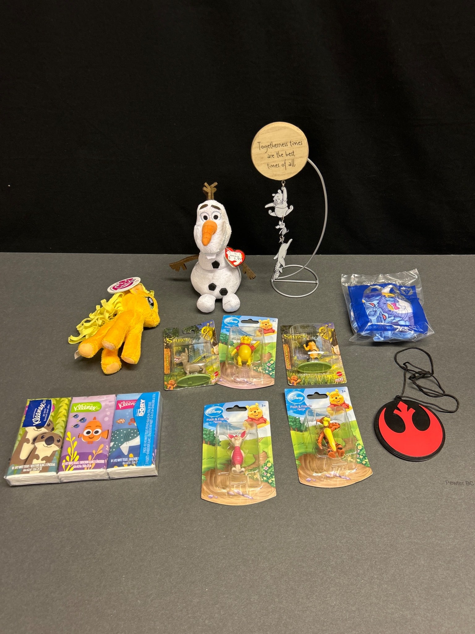 Disney-Themed Toys, Figurines, and Accessories: Various Disney-themed items: a plush Olaf toy with TY tag, a plush My Little Pony figure, a metal display stand with 'Togetherness Times' sign, three themed Kleenex packs, five packaged Winnie the