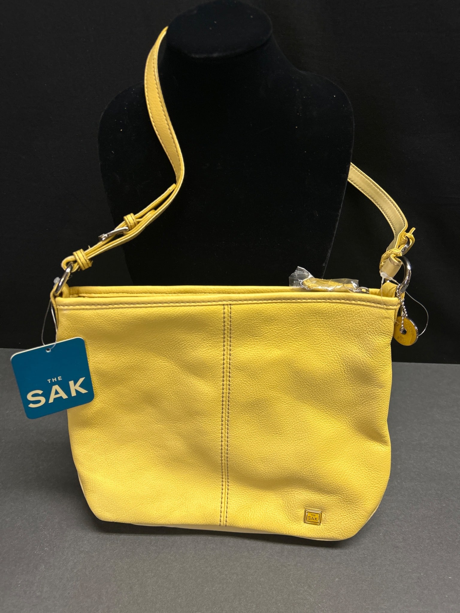 The Sak Yellow Leather Shoulder Bag with Adjustable Strap and Interior Pockets: The Sak yellow leather shoulder bag featuring a visible logo plaque on the exterior and an adjustable strap. The bag includes a zip-top closure, rear slip pocket, interior zippered pocket, and