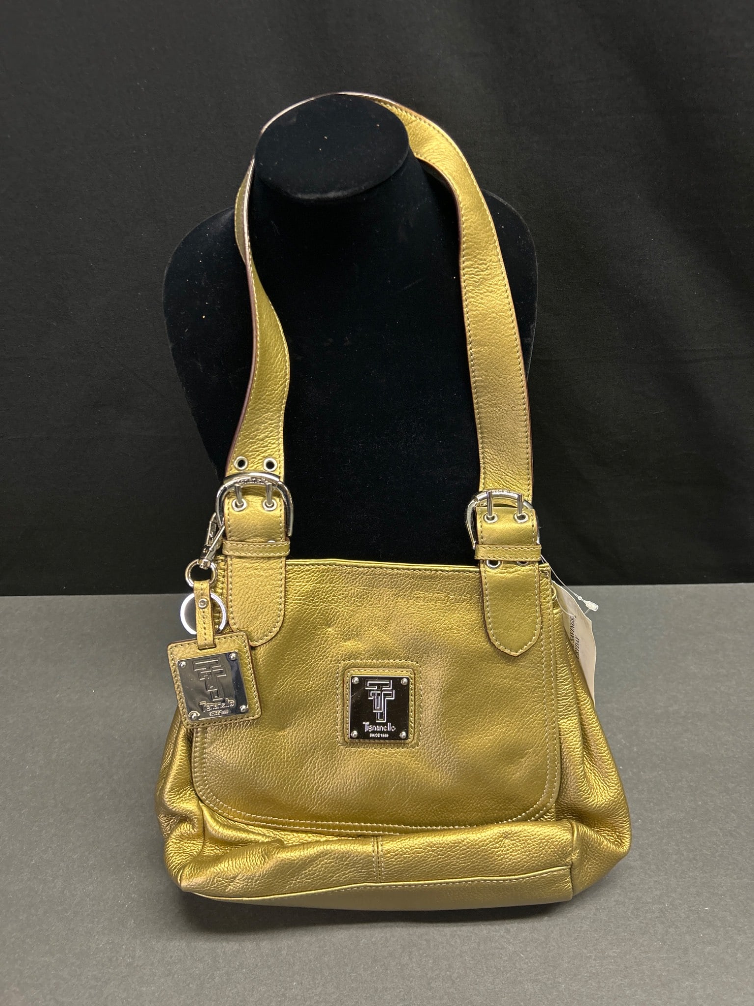 Tignanello Metallic Gold Leather Handbag with Shoulder Straps: Tignanello handbag in metallic gold leather with dual shoulder straps, featuring a front plaque with Tignanello branding and 'Since 1989.' The bag includes a zippered back pocket and a magnetic snap
