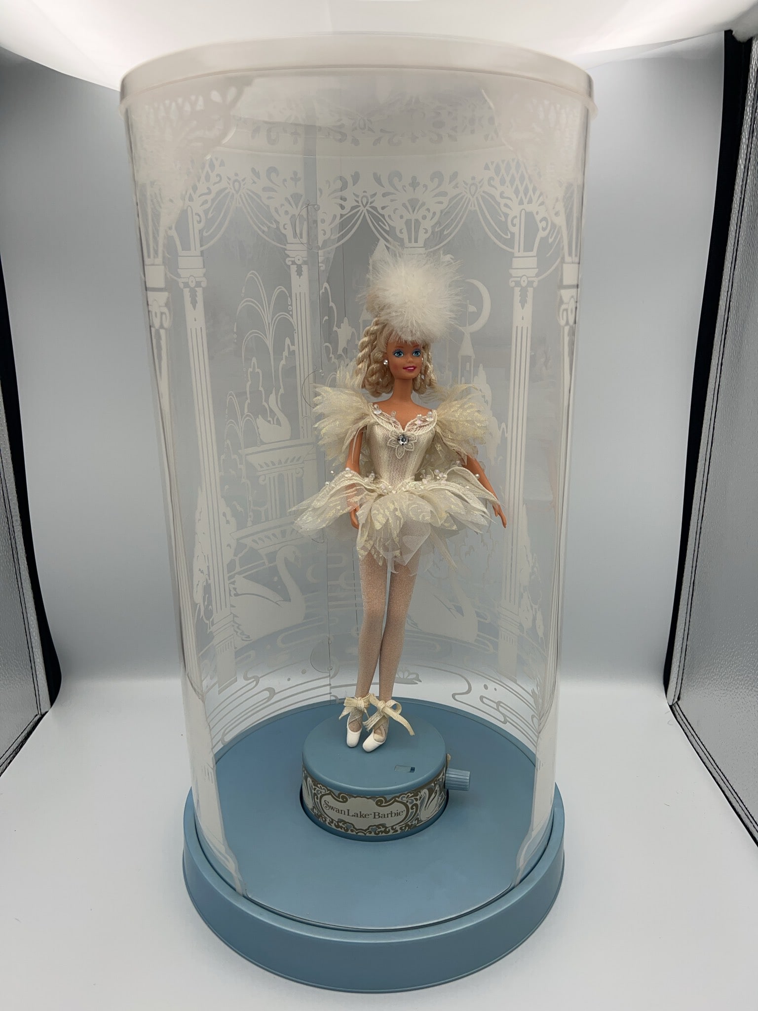 Barbie Swan Lake Ballet Doll in Display Case: Barbie Swan Lake version, functioning, in a decorative cylindrical display case with etched designs. Features detailed ballet costume, feathered headdress, and labeled base. Includes original base
