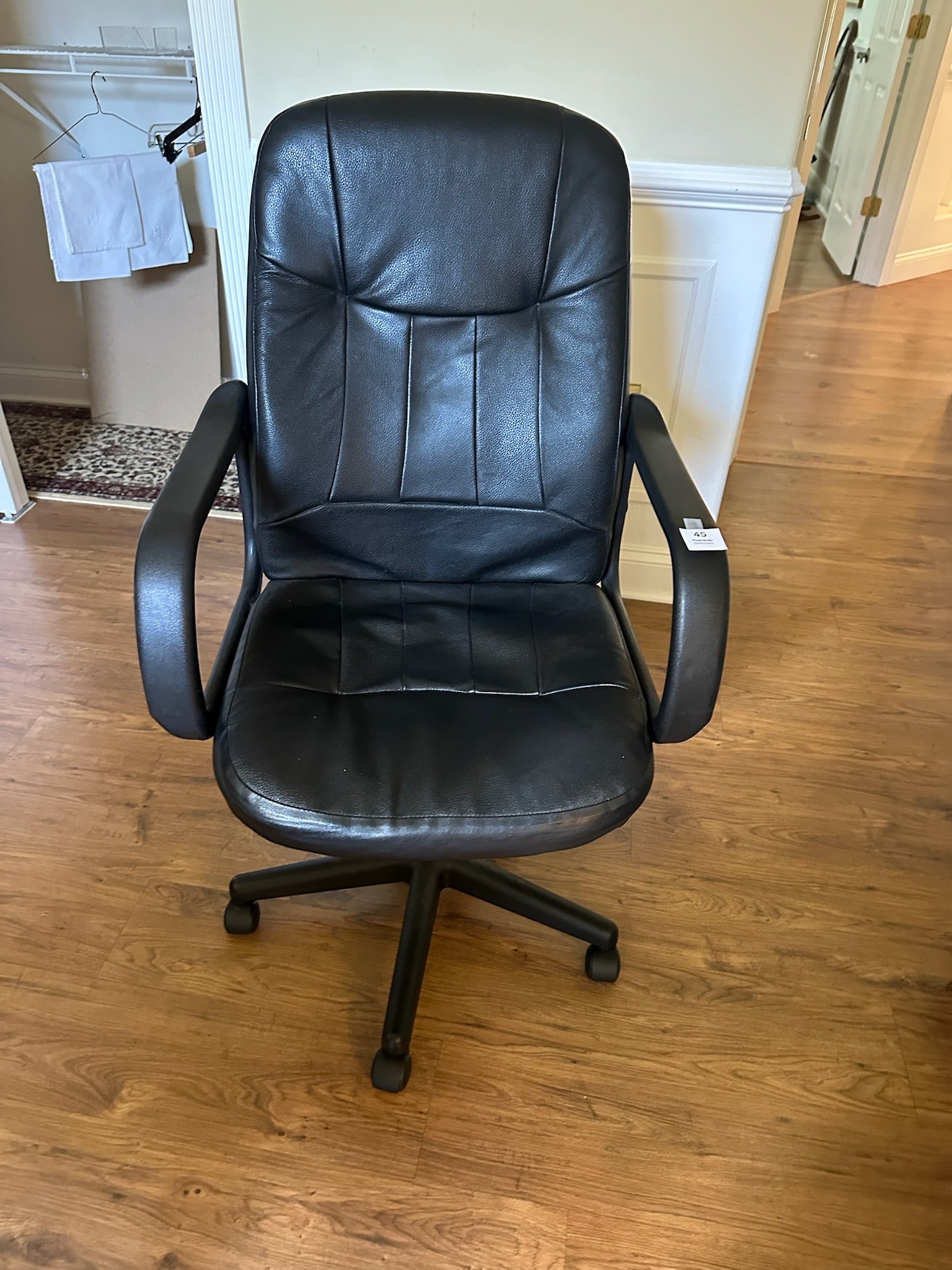 Black Leather Office Chair: Comfortable and practical black faux-leather office chair on rolling base. Features padded seat, backrest, and arms for support, with a swivel and tilt design. Perfect for home or office use.
