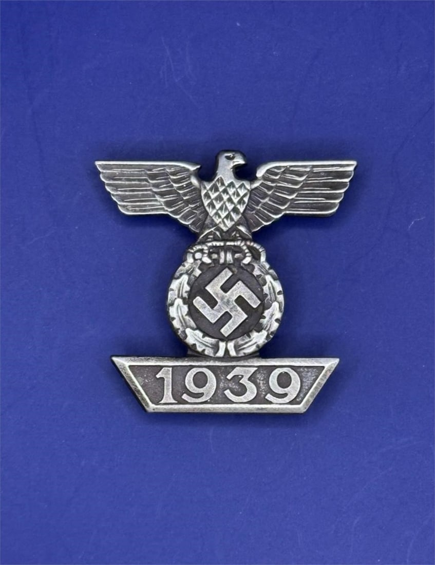 WWII German Clasp to the Iron Cross: Dimensions: 1inThe clasp features a German eagle clutching an oak leaf wreath surrounding a swastika, positioned above a trapezoidal bar with the year "1939".