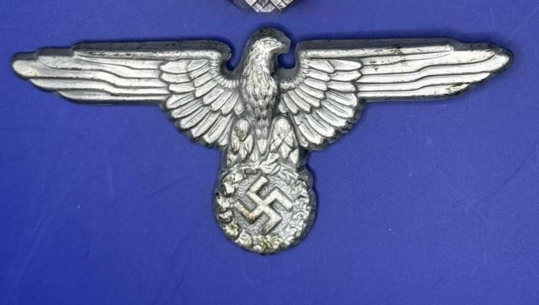 WWII German M1/72 SS Visor Cap Eagle: Dimensions: 3in x 1inConstructed of cupal, the obverse consisting of an SS-style German national eagle clutching a wreathed mobile swastika, the reverse marked with a Reichszeugmeisterei (RZM) logo an