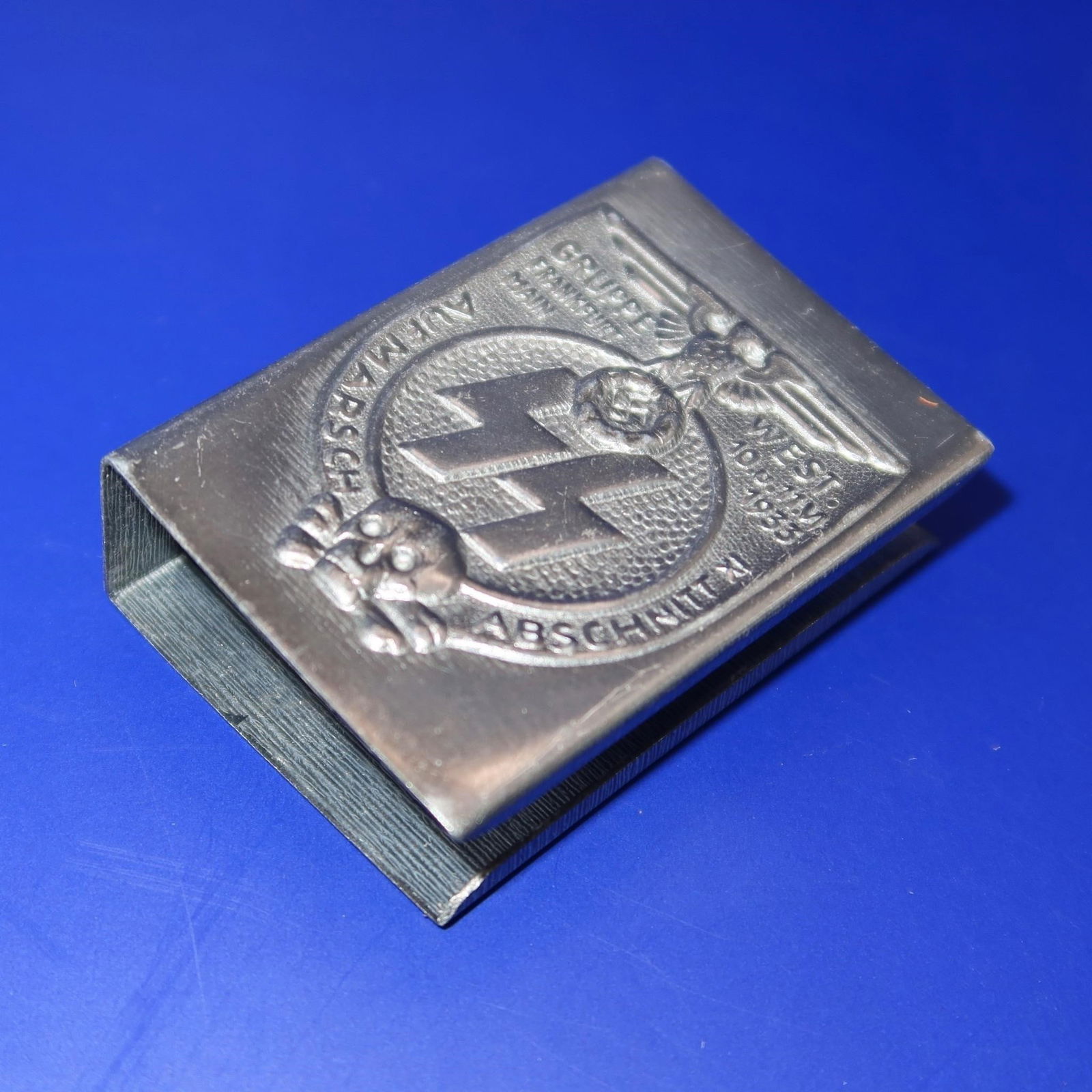 LAH Panzer Division Officer Matchbox Holder: Grey tin matchbox holder with green-grey varnished finish, well-preserved and possibly unused. Measures approximately 51 × 37 × 17 mm (2" × 1 4/8" × 5/8"). Reverse stamped GES SS GESCH. Excellent