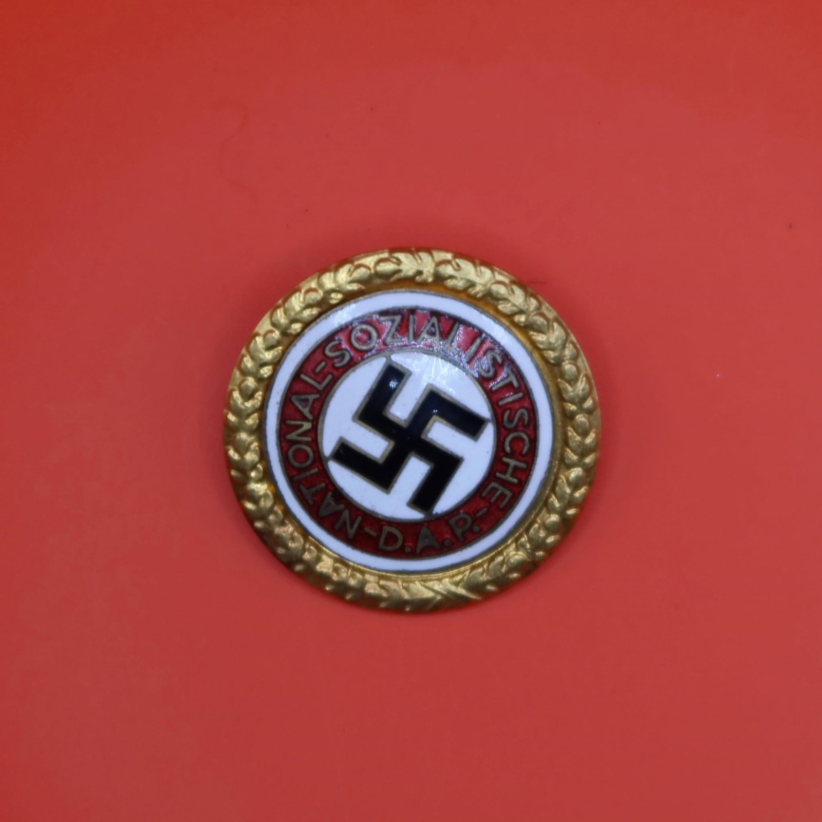 NSDAP Golden Party Badge: Gilded tombak badge with multi-colored enamels, featuring an oak-leaf wreath surrounding a white enameled center with black swastika, encircled by a red enameled band bearing the gilt inscription "NAT