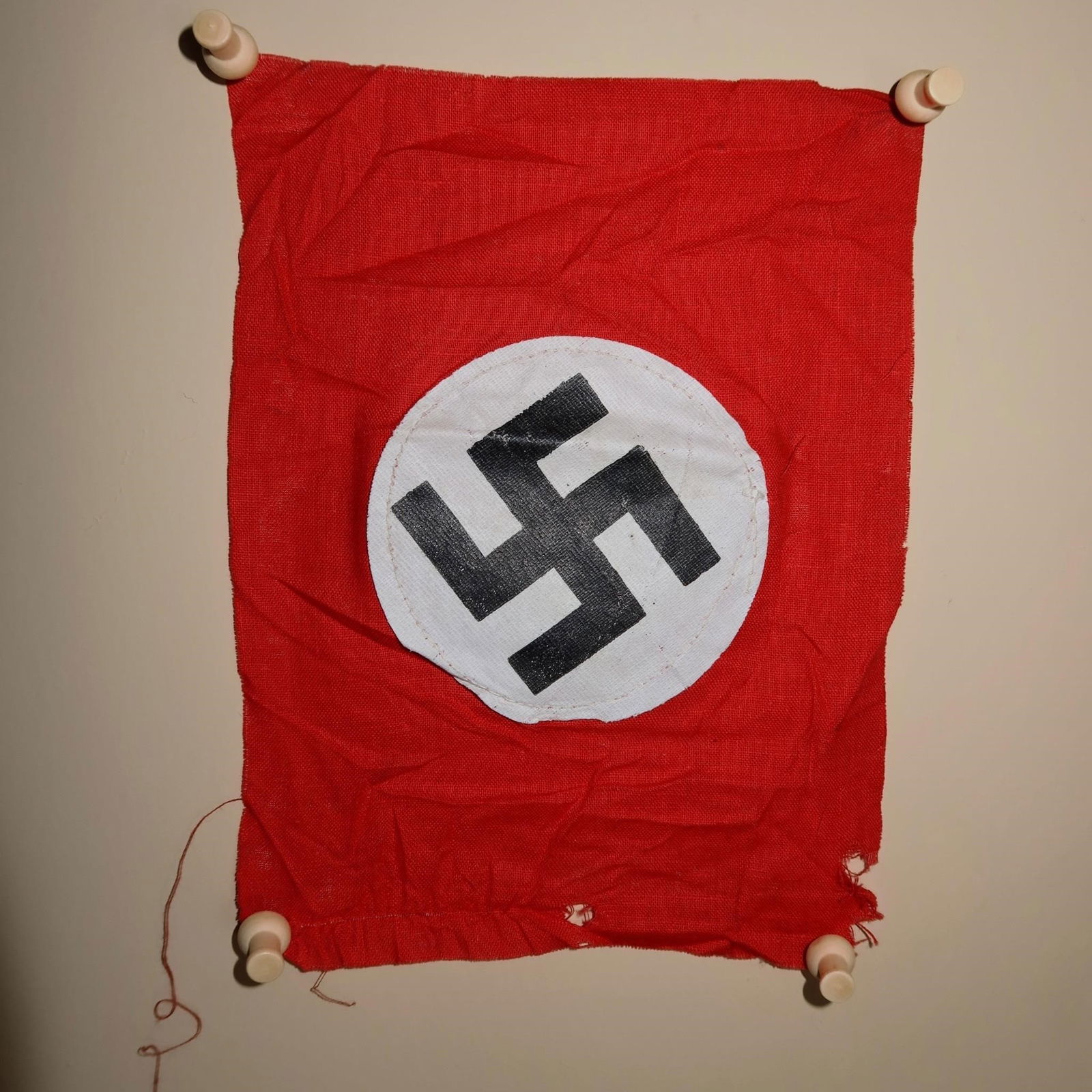 German Party Armband: Red cloth armband featuring a white circular roundel with a black angled swastika at the center. Constructed of woven fabric with finished edges. Measures approximately 7.5 × 6.7 inches.