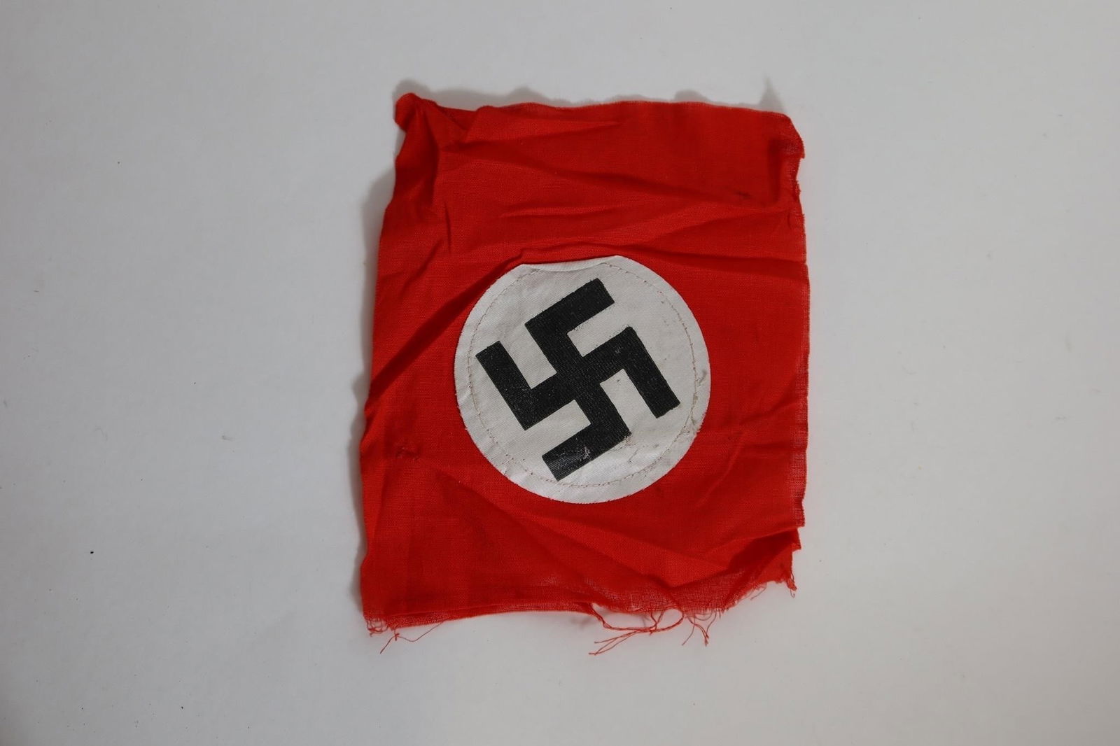 WWll German Party Armband: Two sided red cloth armband featuring a white circular roundel with a black angled swastika at the center. Constructed of woven fabric with finished edges. Measures approximately 7.5 × 6.7 inches.