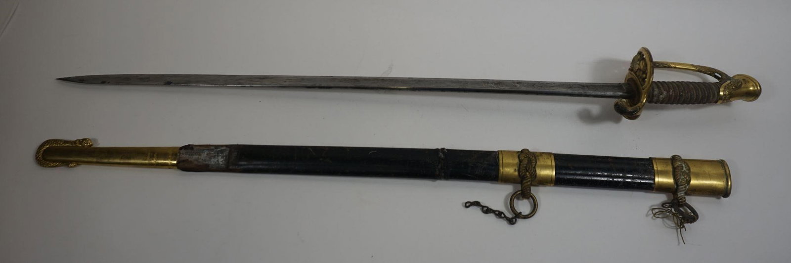 US Navy 1852 Military Officer's Cutlass Sword: The US Navy Officer Sword is a ceremonial blade, often called a saber, with a stainless-steel, acid-etched blade, a brass guard featuring USN, an ivory-like grip, and a leather-covered scabbard. The h