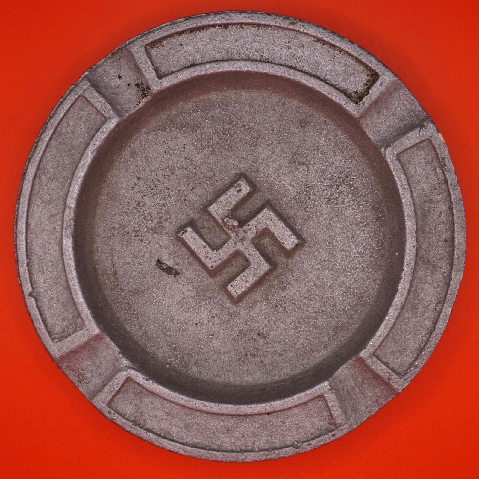 WWII German Wehrmacht Ashtray: Original WWII-era German ashtray featuring a central swastika emblem, associated with the Wehrmacht period. Constructed of cast metal with a simple circular form and segmented rim.