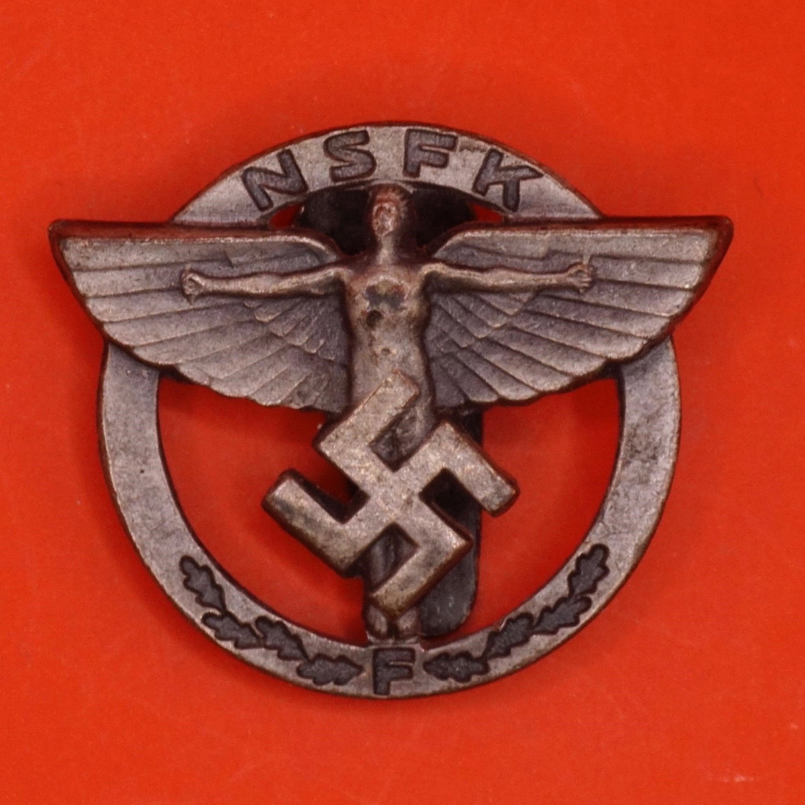 German NSDAP NSFK Sponsoring Member Badge: Original German NSDAP NSFK 21mm sponsoring member pin (Förderer-Abzeichen), alloy, winged Icarus with swastika and "F" on oak-leaf spray, embossed "Ges. Gesch." on reverse, original pinback intac