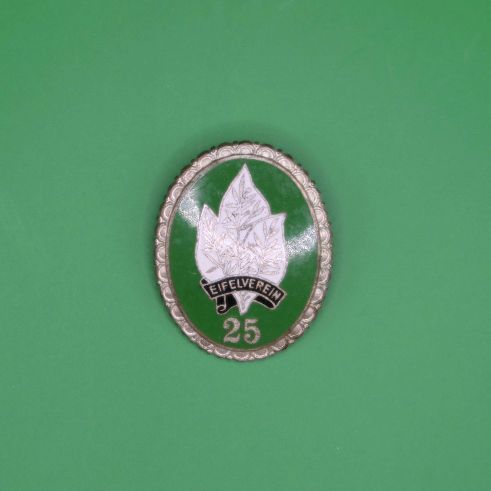 Eifelverein 25-Year Membership Badge: This is a 25-year service badge from the Eifelverein, a long-established German hiking and nature-preservation organization founded in 1888. The front shows a green enamel field with a white multi-lea