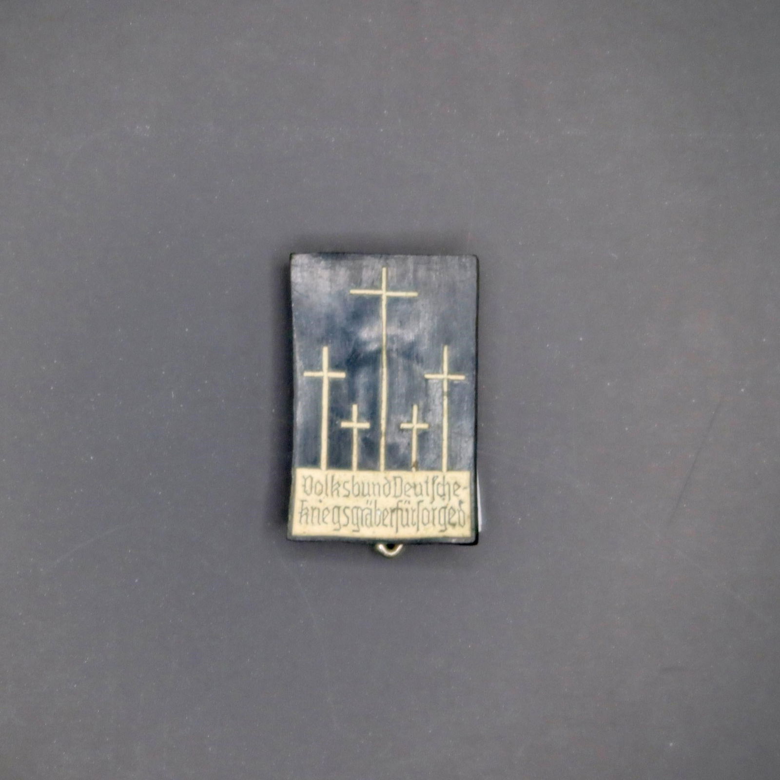 Volksbund War Graves Support Pin: A small rectangular badge showing five simple crosses rising from a dark background, symbolizing military graves. Along the bottom is the inscription "Volksbund Deutsche Kriegsgräberfürsorge". It's