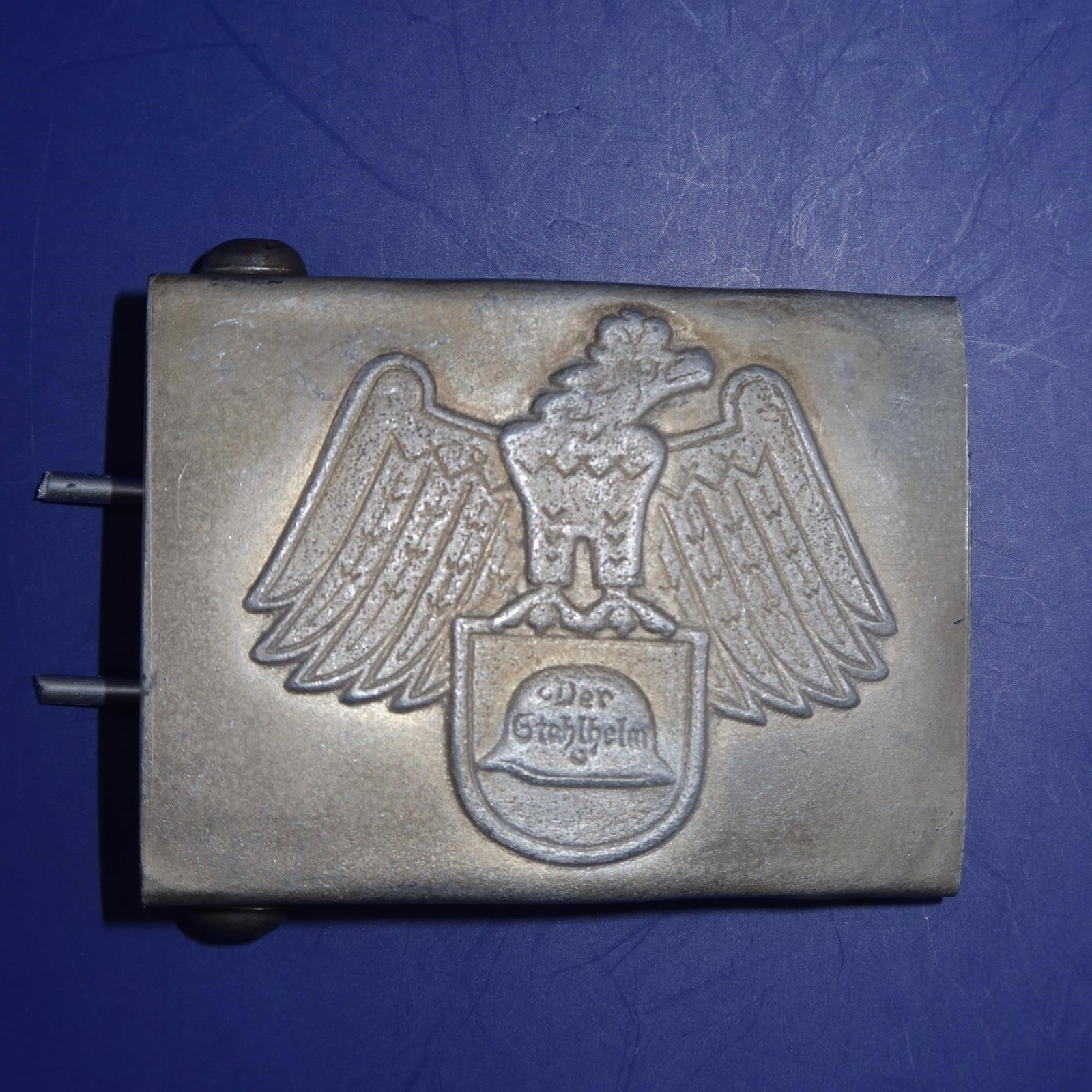 Der Stahlhelm Member's Belt Buckle: Constructed of dark grey-painted magnetic metal, the obverse displaying a raised crowned German national eagle grasping a Stahlhelm emblem. The reverse features a belt loop with dual attachment