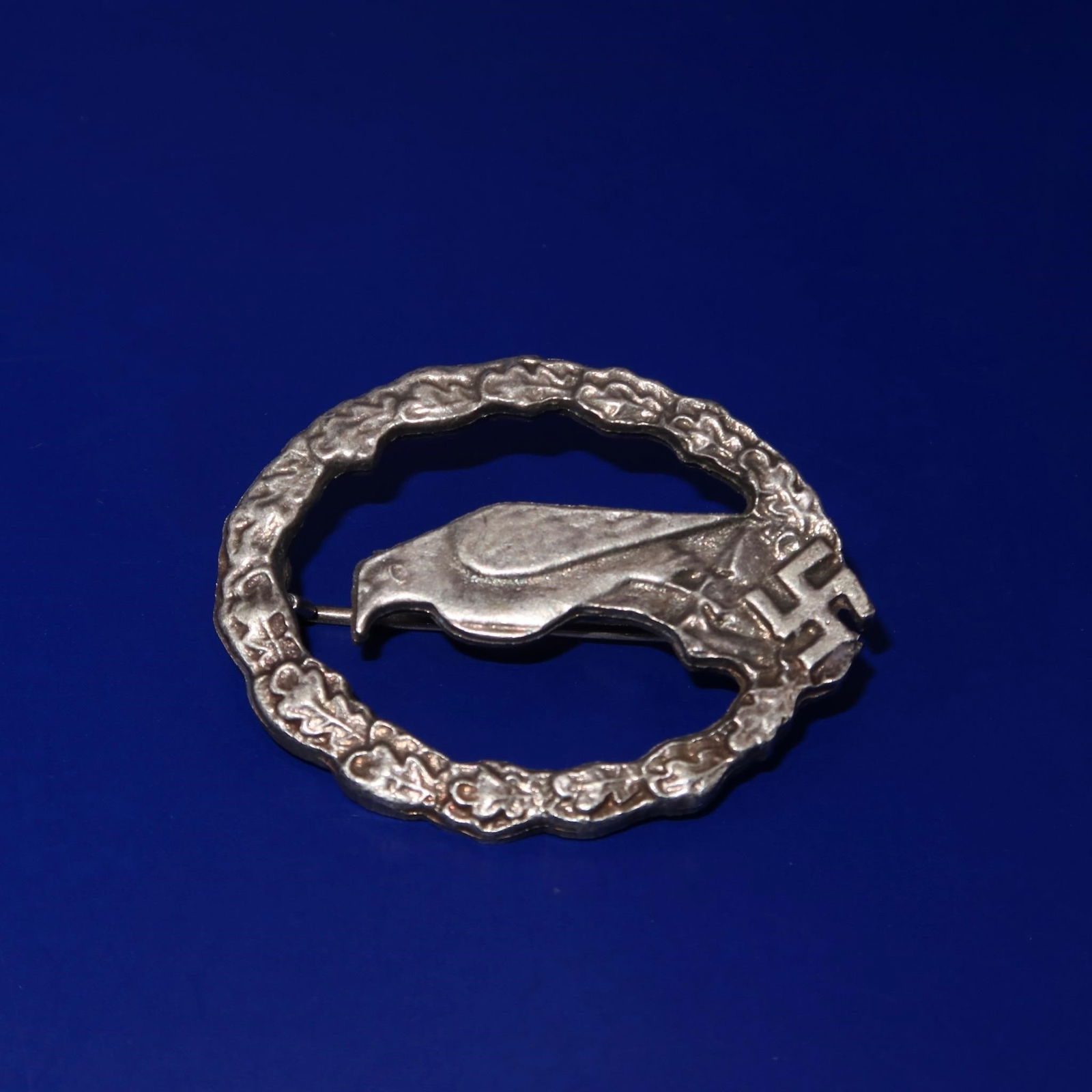 Luftwaffe Retired Pilot's Badge: A Luftwaffe Retired Pilot's Badge featuring a three-dimensional design with a perched eagle displayed at the center, encircled by a laurel-and-oakleaf wreath. At the bottom center of the wreath is a