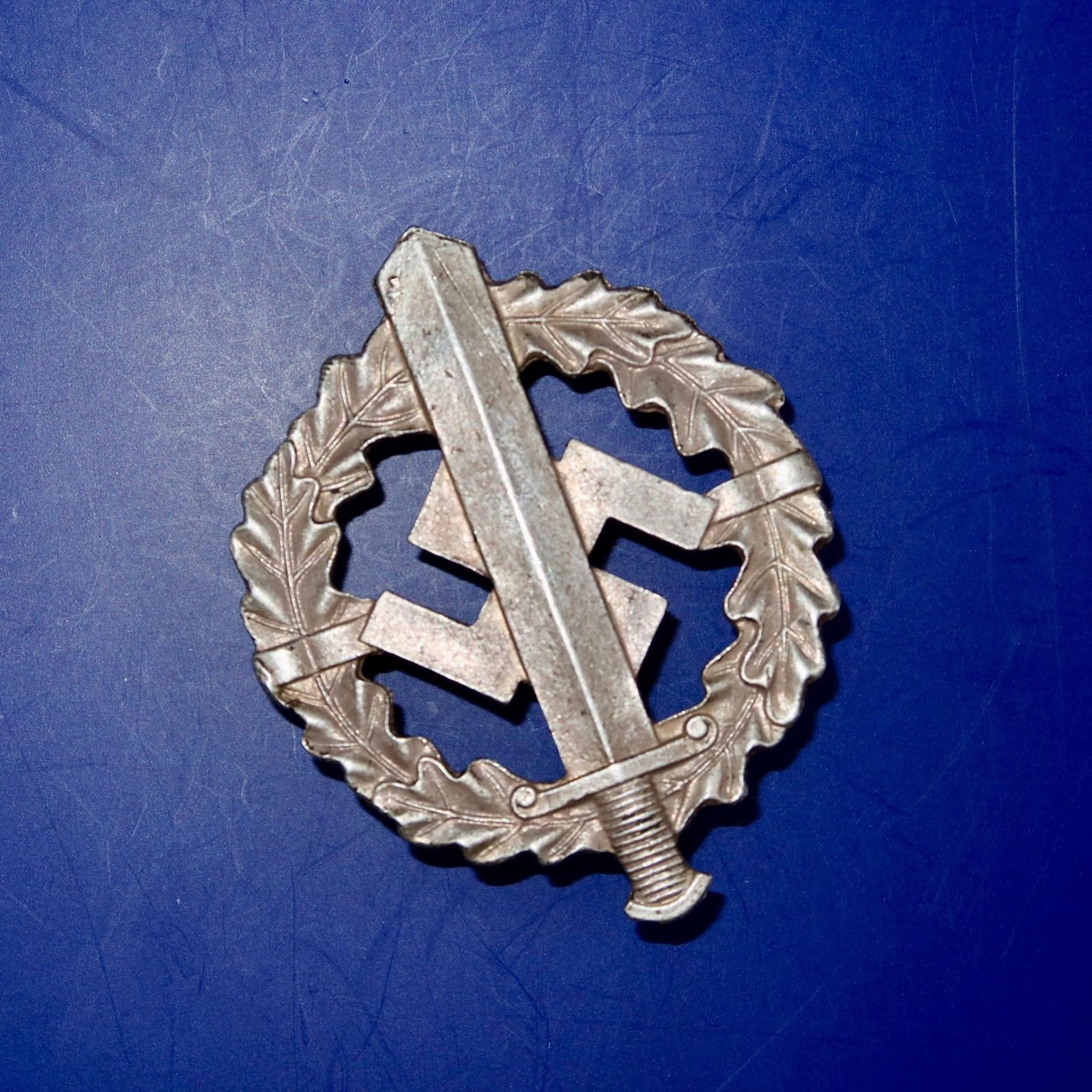 German NSDAP SA/SS Sports Badge in Bronze: Die-struck, magnetic sheet-metal badge with bronze wash finish. Circular oak-leaf wreath enclosing an upward-pointing Roman broadsword superimposed over a canted swastika. Detailing includes veined