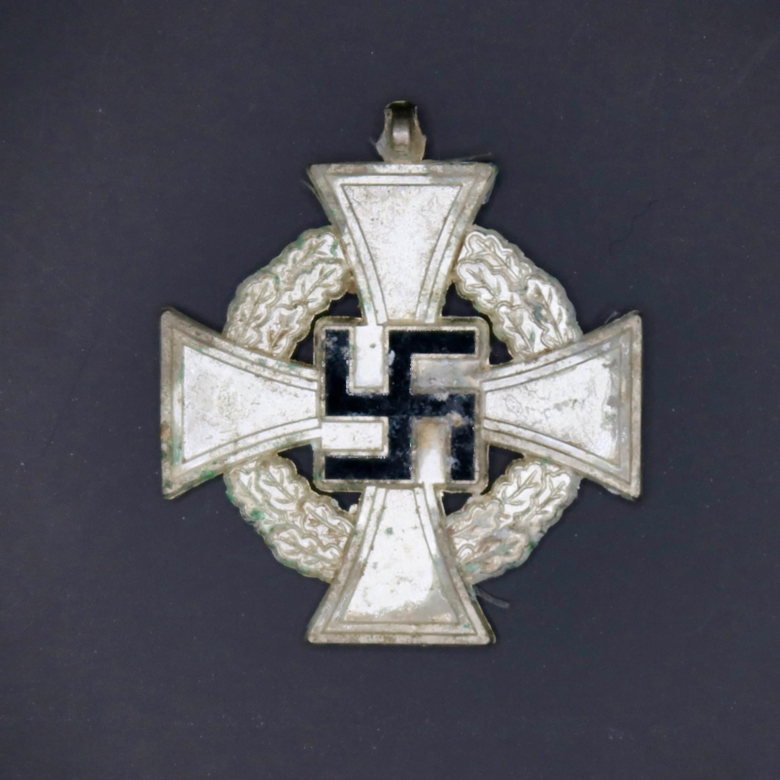 Original 25-Year National Faithful Service Medal: Silvered bronze medal with blue ribbon, measuring approximately 41 × 41 mm. The obverse displays a silver cross with a black enamel swastika at its center, surrounded by an oak wreath. The reverse