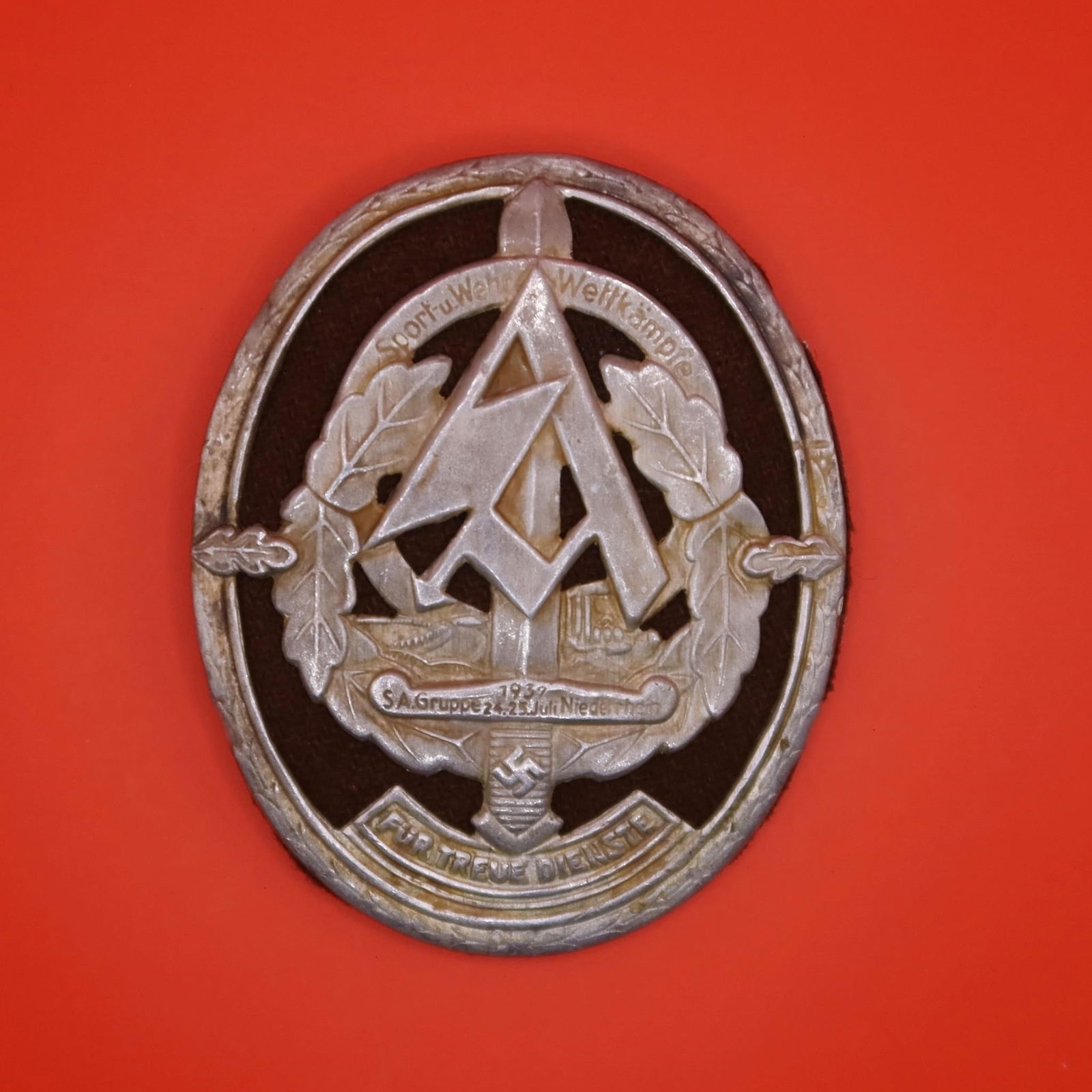 WWII German SA Deployment Badge: WW2 German SA Deployment Badge. Silvered alloy metal with a red rayon material insert. Safety pin attachment system on back, four tabs attaching front section to backing plate. Worn condition.