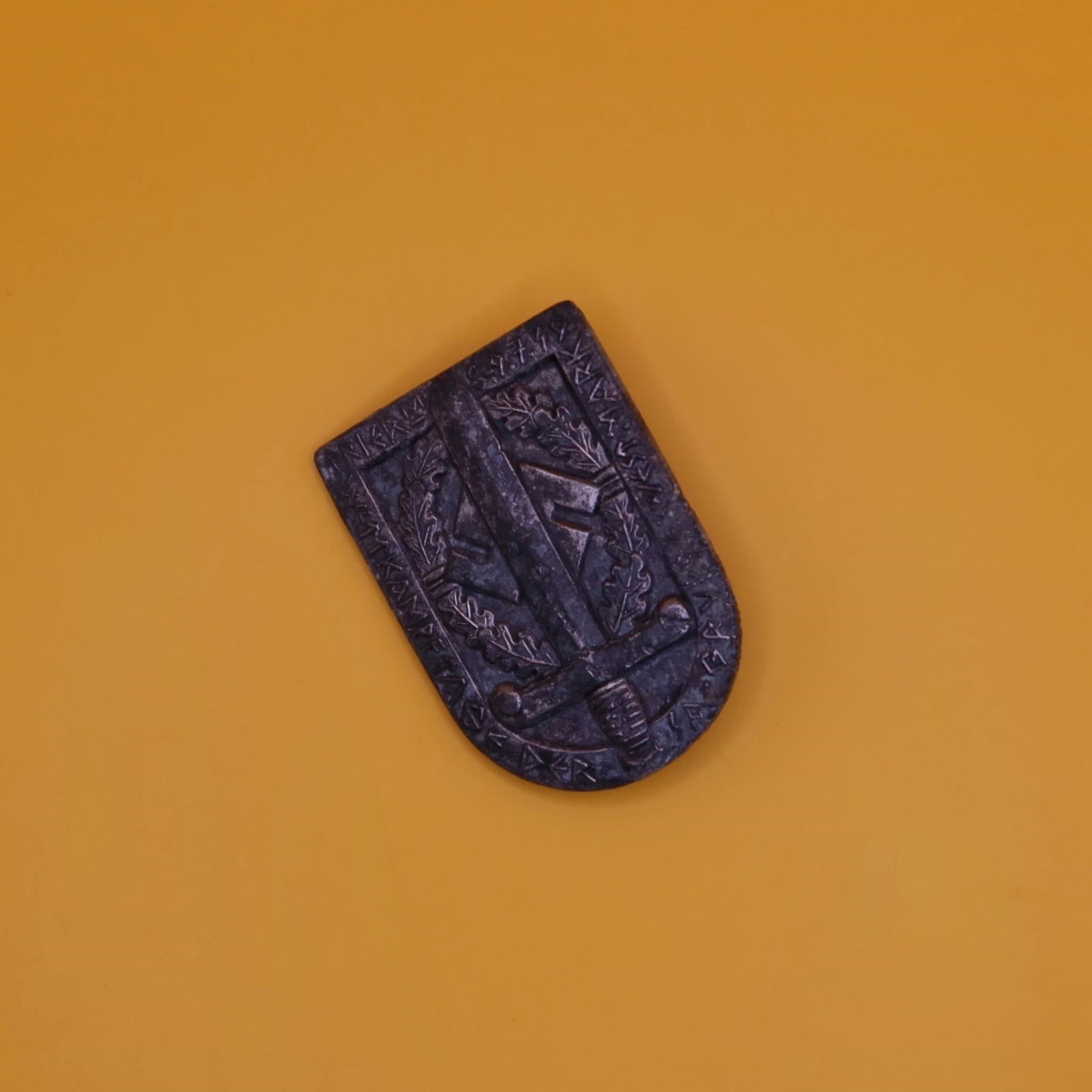 German WWII SA Sports Badge: Shield-shaped aluminum badge with dull grey finish, featuring the SA sports emblem of a vertical broadsword over a swastika within a laurel wreath, surrounded by the inscription "WETTKÄMPFE DER