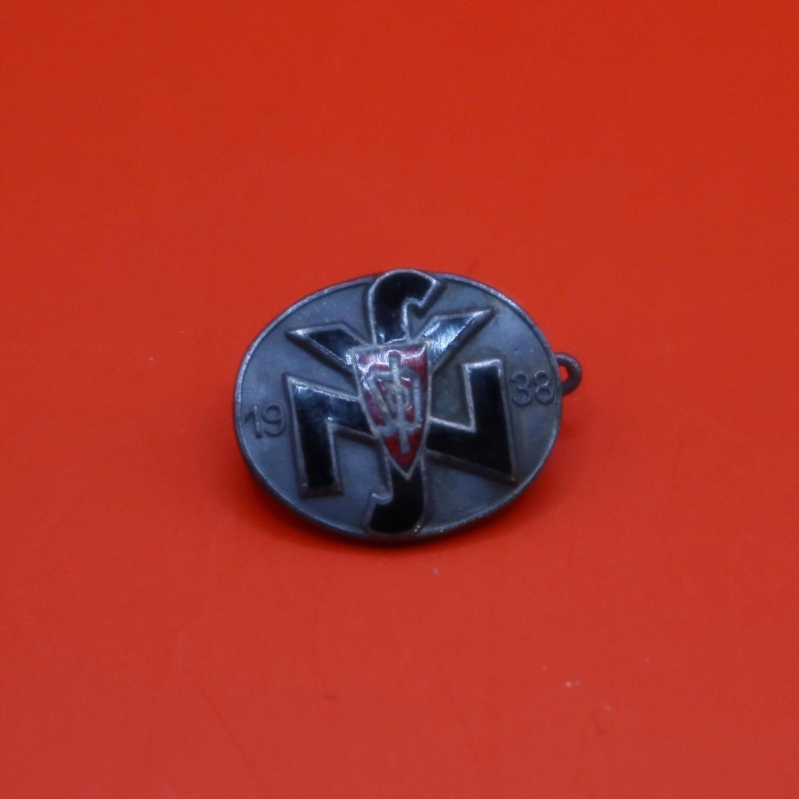 Sudeten Party / NSV Badge (1938): Silvered bronze badge with red and black enamels, depicting the Sudeten Party insignia over a National Socialist People's Welfare emblem, flanked by "19" and "38" (1938). Horizontal pinback with dark