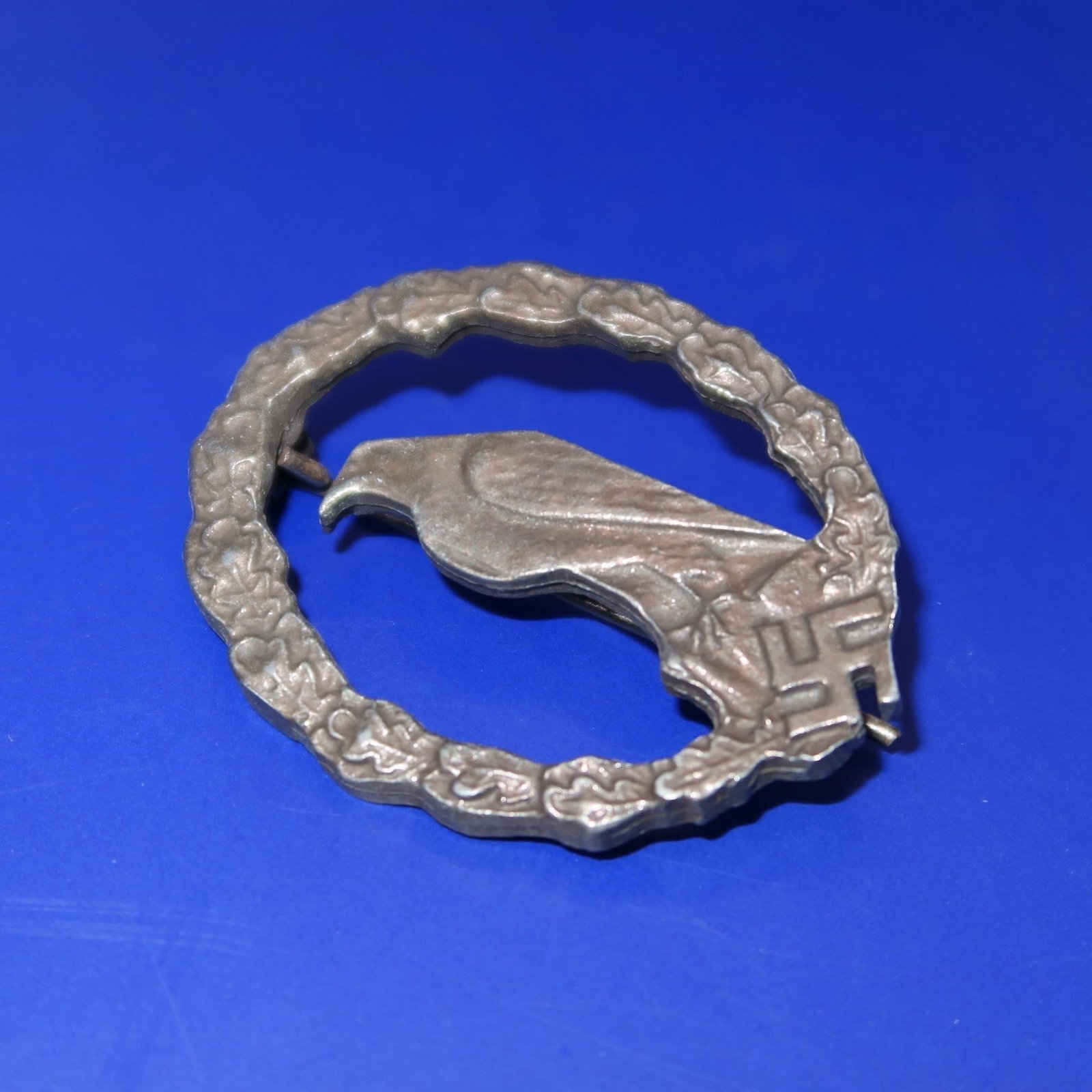 Luftwaffe Retired Pilot's Badge: A Luftwaffe Retired Pilot's Badge featuring a three-dimensional design with a perched eagle displayed at the center, encircled by a laurel-and-oakleaf wreath. At the bottom center of the wreath is a