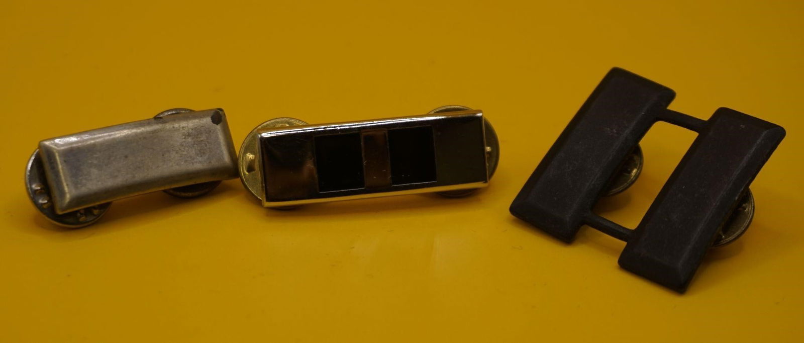 WWII US Army Captain Rank Insignia Pins: These are U.S. Army Captain rank insignia pins. The silver-colored pin on the left appears to be a worn or older version of the rank. The polished pin in the center is a standard, modern U.S. Army