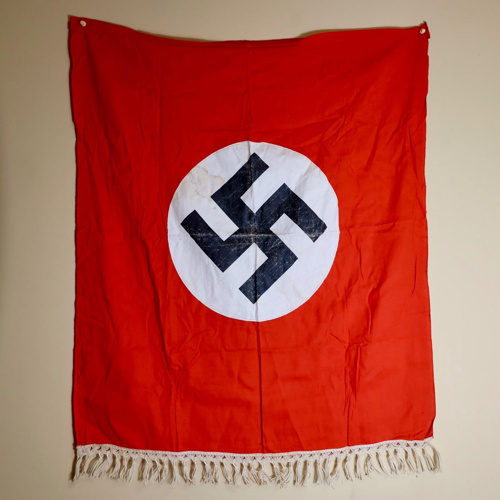 Third Reich-Era German Red Flag: Rectangular red cloth flag with a white circular roundel at the center, bearing a black angled swastika. Finished with a white fringe along the bottom edge. Measures approximately 37 × 30 inches.