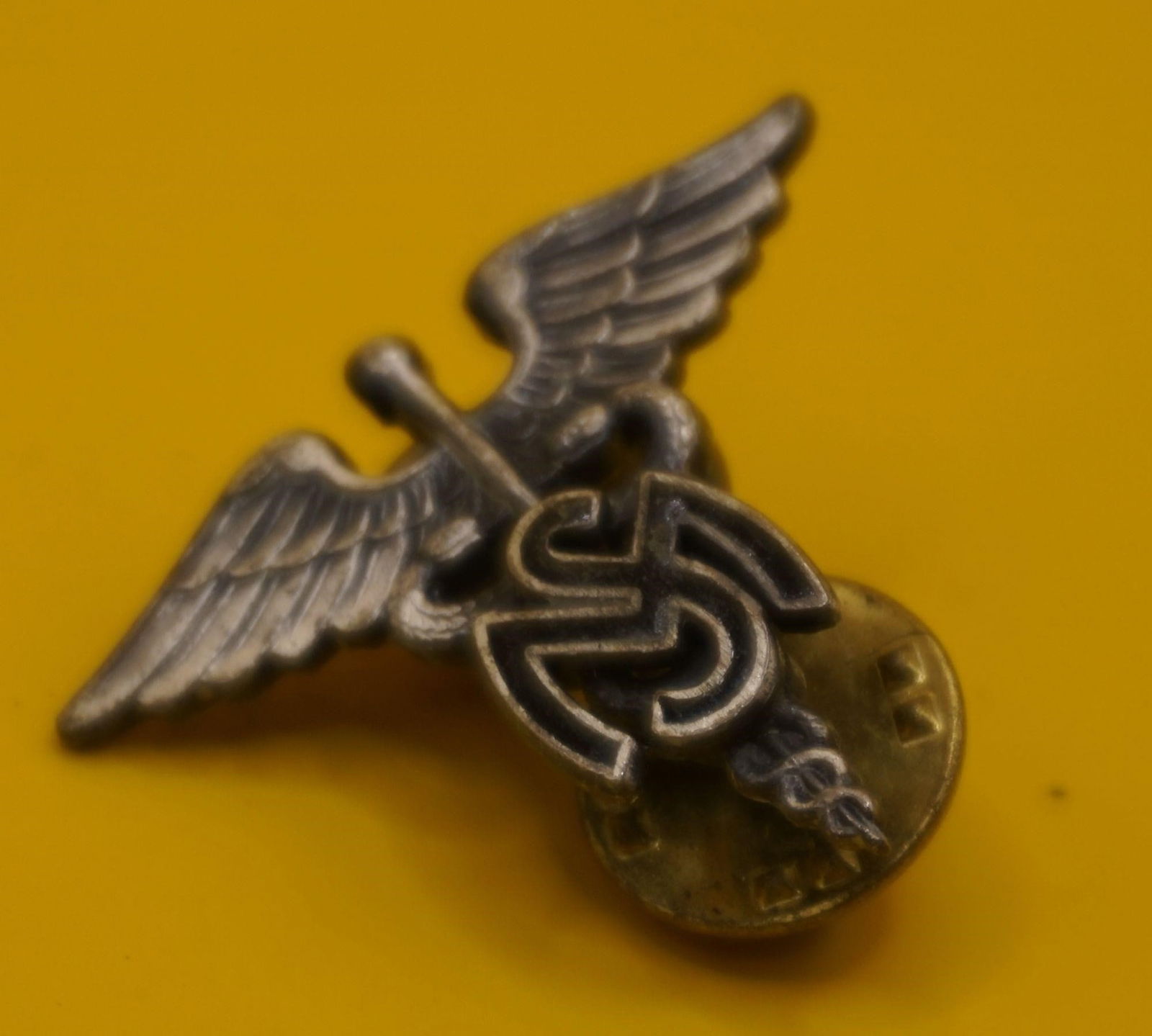 WWII US Army Medical Service Corps Insignia Pin: The insignia features a caduceus, which has been used by the Army Medical Department since 1851. The current design has remained unchanged since 1902. The Medical Service Corps was established in the