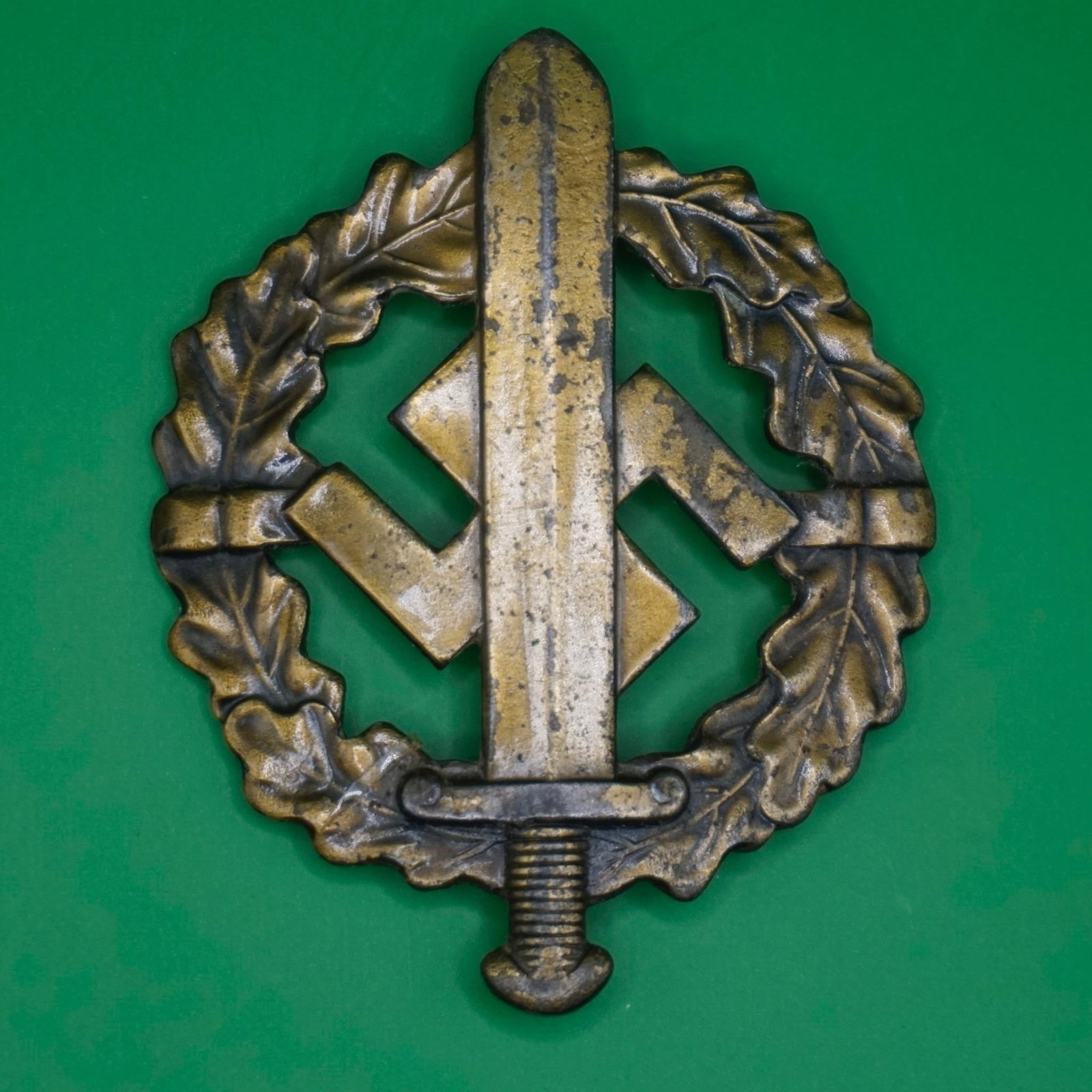 Original German SA Sports Badge in Bronze: Original WWII-era German NSDAP SA/SS Sports Badge (SA-Sportabzeichen) in bronze, die-struck magnetic metal with bronze wash, oak-leaf wreath and sword over swastika design. Reverse marked "Eigentum de