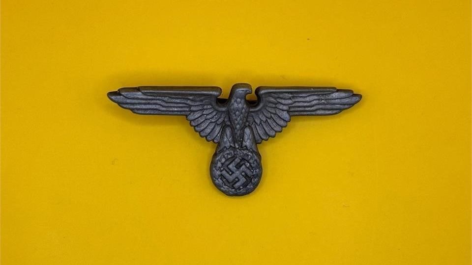 WWII German SS Officer Visor Cap Eagle: Introduced in 1936, the SS visor cap eagle replaced earlier designs to distinguish SS officers from the SA. Worn throughout World War II, it identified SS affiliation and rank, symbolizing the organiz