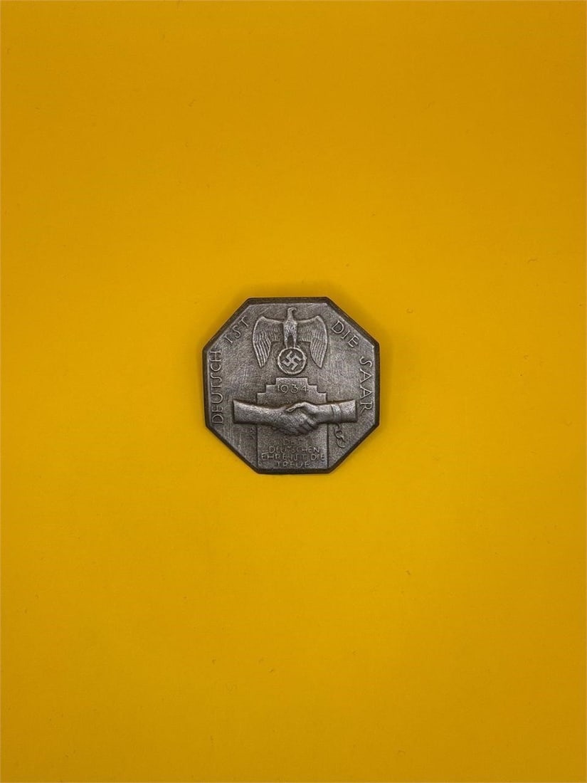 1934 NSDAP "Deutsch ist die Saar" Badge: Issued in 1934, this NSDAP badge commemorated the Saar region's return to Germany. It features an eagle clutching a wreathed swastika above two shaking hands, symbolizing unity and loyalty, and was
