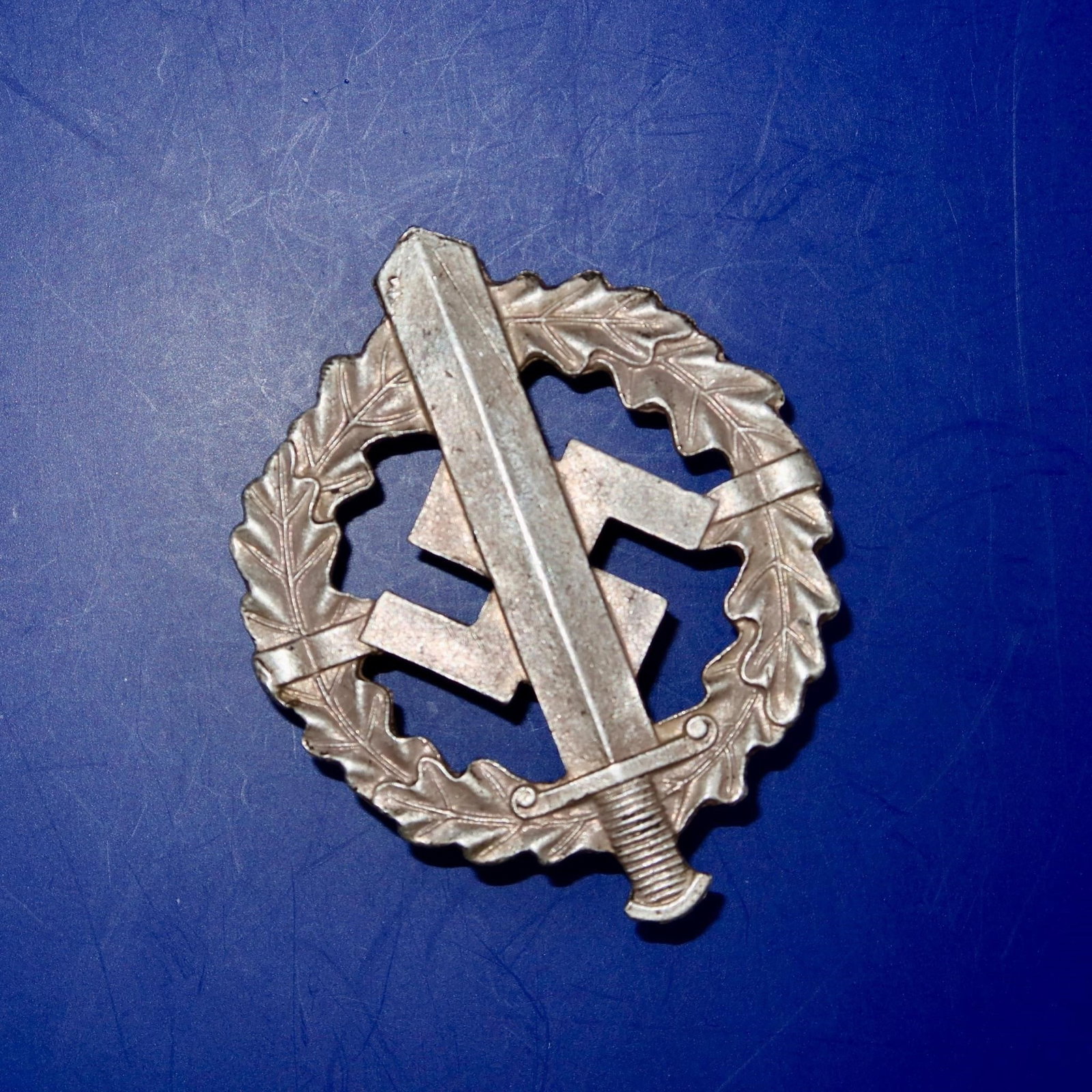 German NSDAP SA/SS Sports Badge in Bronze: Die-struck, magnetic sheet-metal badge with bronze wash finish. Circular oak-leaf wreath enclosing an upward-pointing Roman broadsword superimposed over a canted swastika. Detailing includes veined