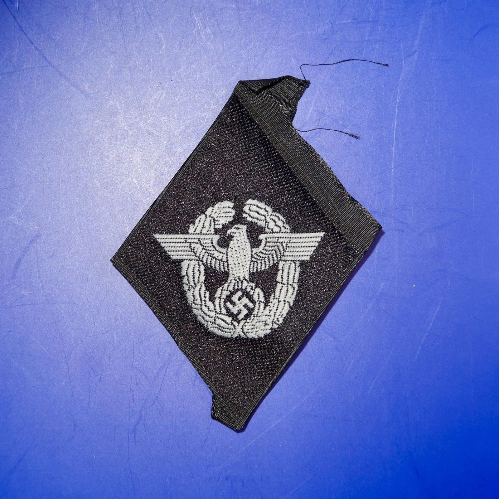 Waffen-SS Polizei Sleeve Diamond: Vertical woven black rayon diamond measuring approximately 65 × 45 mm, featuring a machine-woven police eagle surrounded by a vertically oval oak-leaf wreath in silvery-grey rayon threads. The