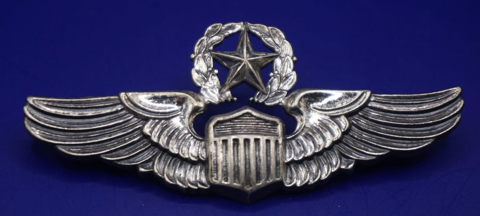 WWII US Air Force Command Pilot Wings Badge: This is a U.S. Air Force Command Pilot Wings badge. The badge features a federal shield centered upon a pair of wings, with a five-point star encircled by a laurel wreath atop the shield. It represent