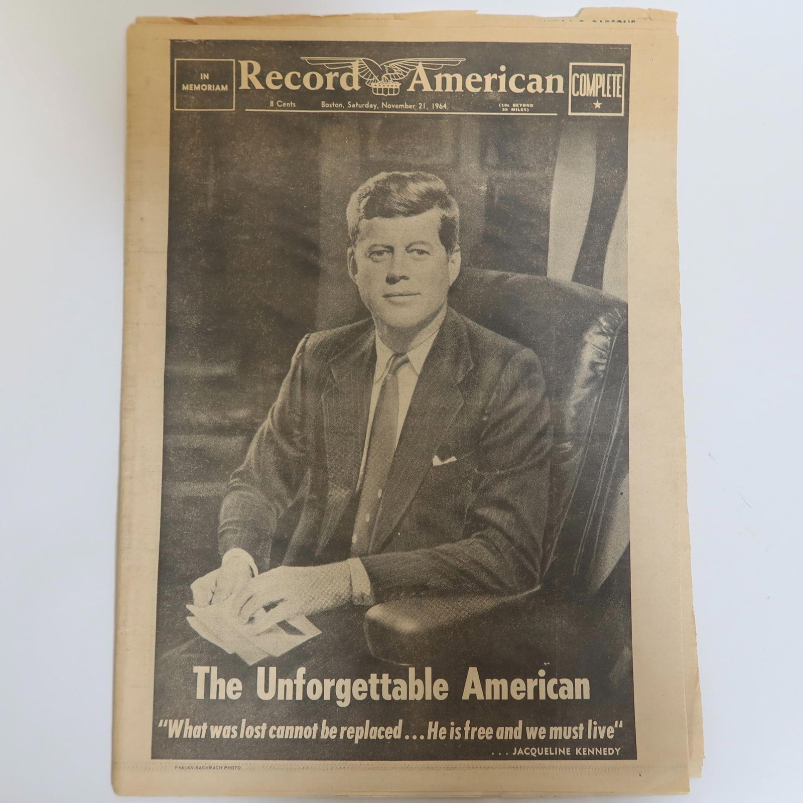 JFK Tribute Newspaper: An original Record American newspaper featuring a full-page John F. Kennedy tribute titled "The Unforgettable American," along with interior coverage including national news, editorials, memorial