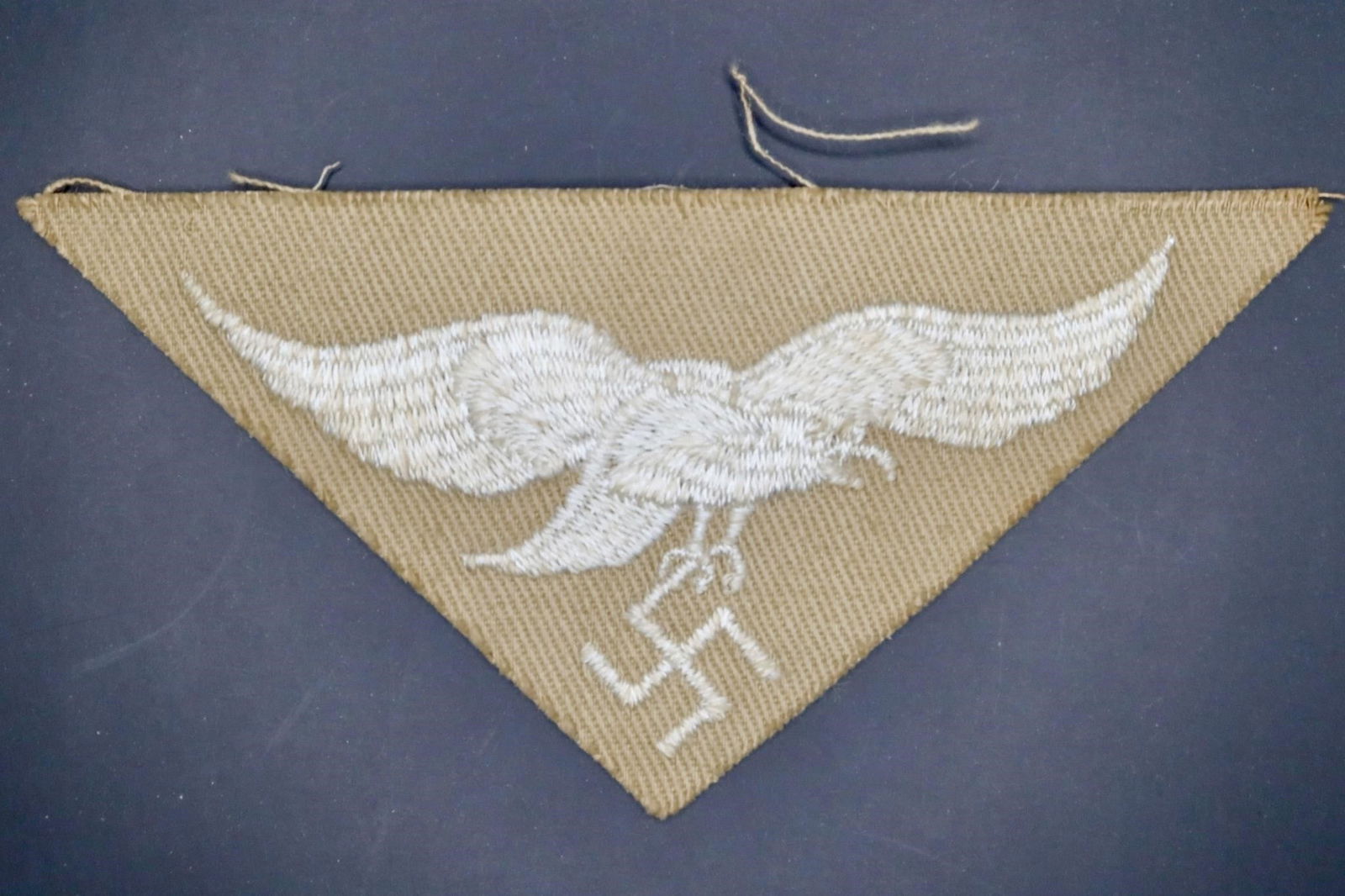 Luftwaffe Africa Corps Tropical Eagle: Machine-embroidered second pattern eagle (circa 1936-1945) in silvery-grey cotton threads on a cut-out, inverted triangular tan cotton base. Measures approximately 83 mm wingspan from tip to tip.