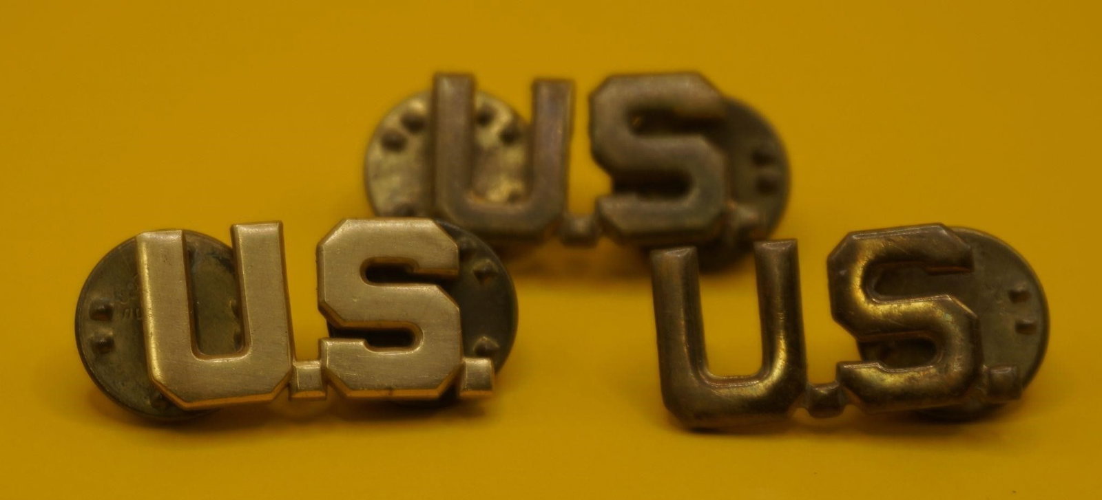 Vintage U.S. Army officer collar insignia pins: These are These are vintage US Army officer collar insignia pins. They feature the letters "U.S." in gold or brass finish. The pins are typically worn on the uniform collar. They are from the World
