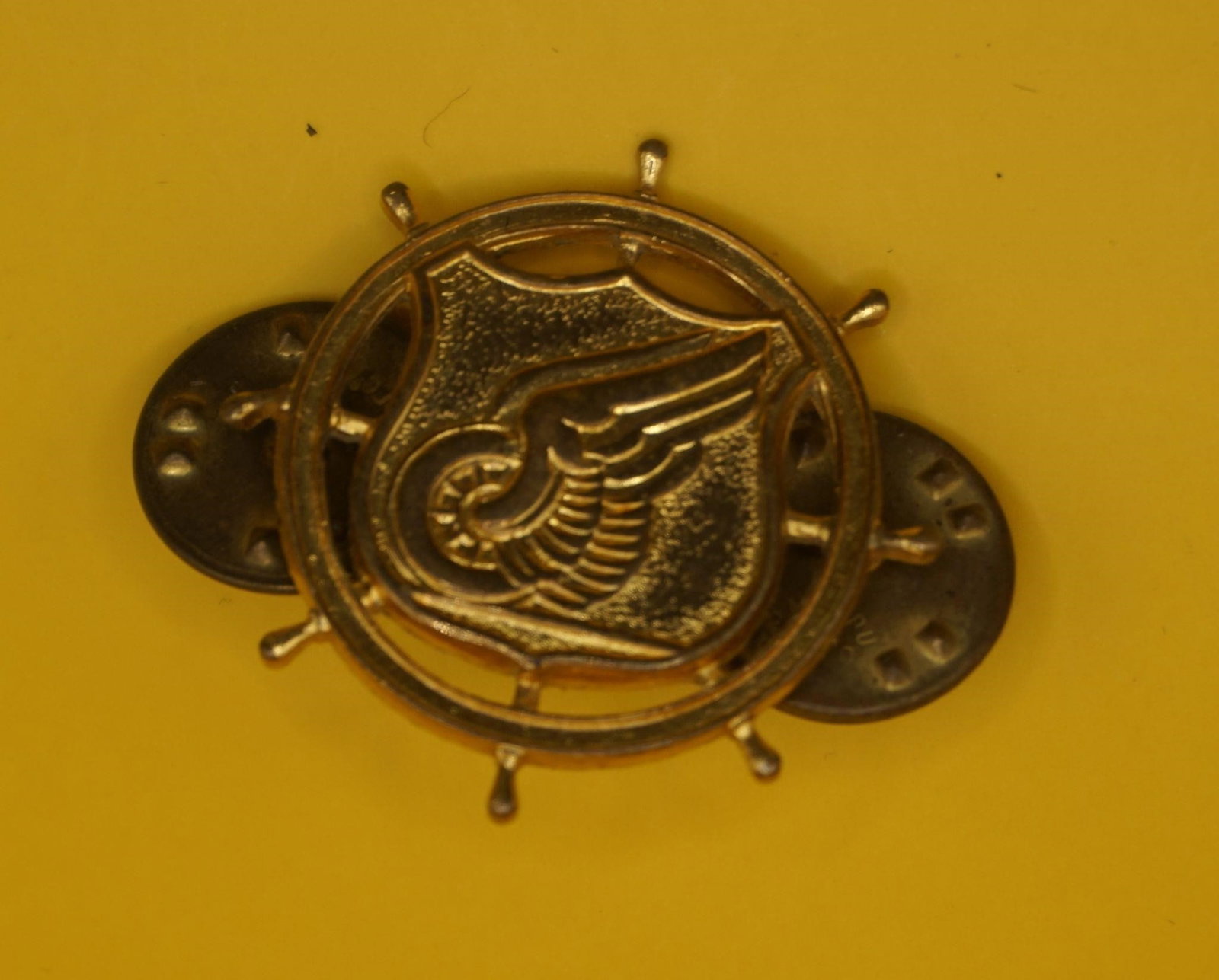 WWII US Army Transportation Corps Insignia Pin: This is a U.S. Army Transportation Corps officer's branch insignia pin, often considered a collectible item. The insignia features a ship's steering wheel, a shield, and a winged car wheel on a rail.
