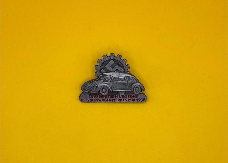 1938 Volkswagen German Workers Badge: This badge commemorates the groundbreaking of the Volkswagen factory in May 1938. Issued to German workers, it features a VW profile beneath a swastika-cog emblem and was produced in nickel with a