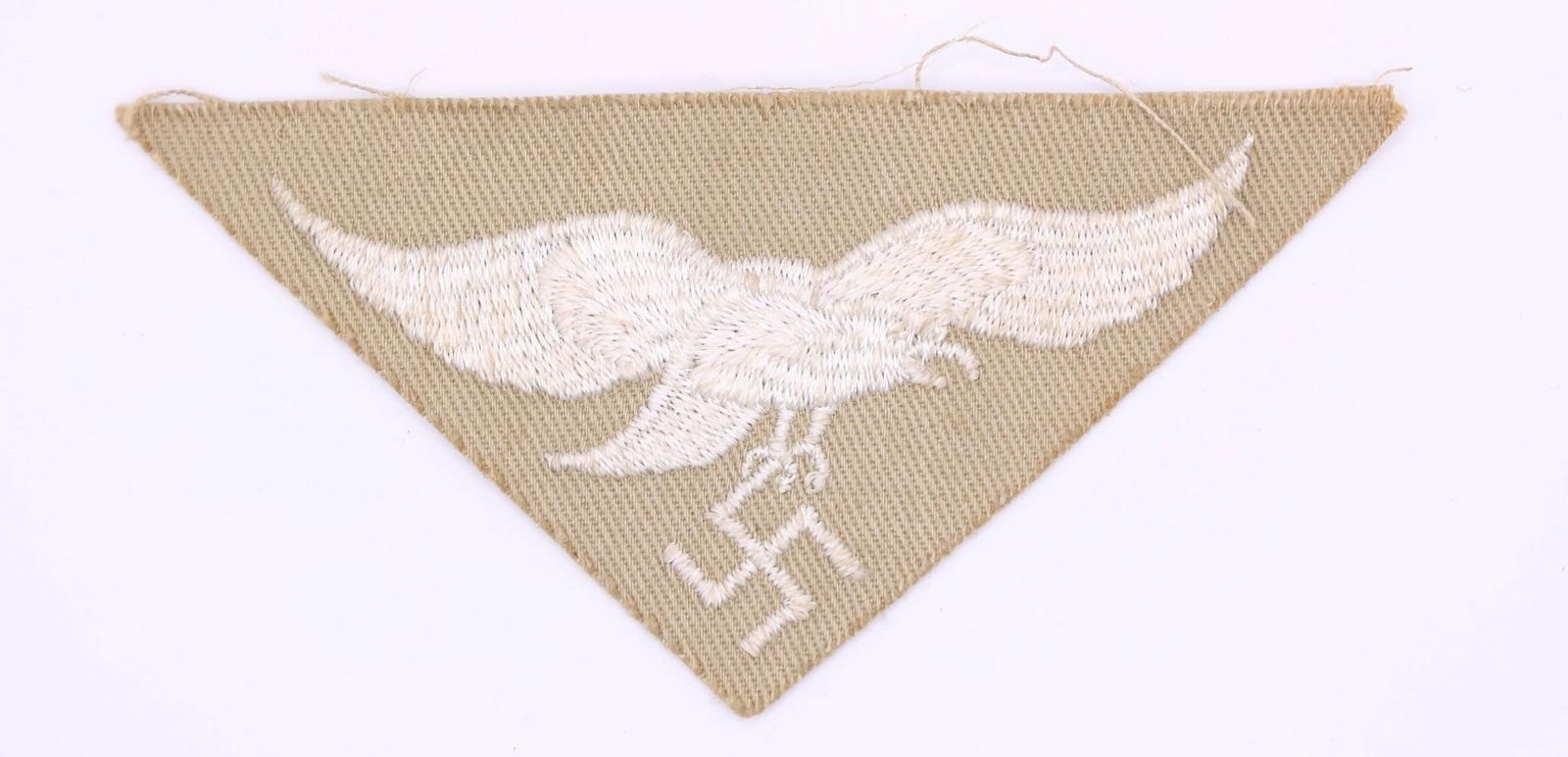 Luftwaffe Africa Corps Tropical Eagle: Machine-embroidered second pattern eagle (circa 1936-1945) in silvery-grey cotton threads on a cut-out, inverted triangular tan cotton base. Measures approximately 83 mm wingspan from tip to tip.