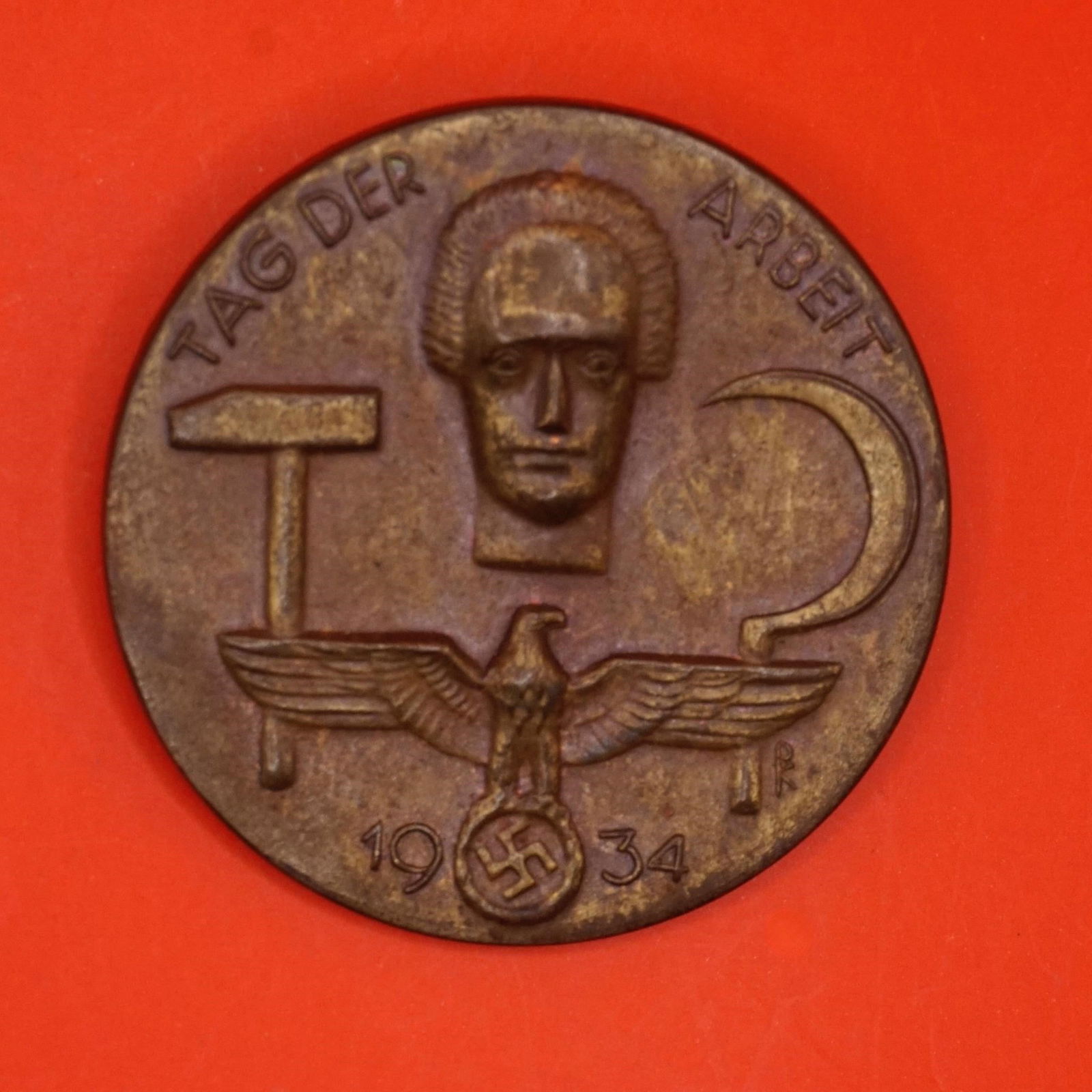 German 1934 Tag der Arbeit Tinnie: Original 1934 German Tag der Arbeit (Labor Day) tinnie, stamped gilt tombac, 35mm diameter, horizontal pin, marked "SCHWAB GMUND 17" on reverse. Very nice condition with detailed design.