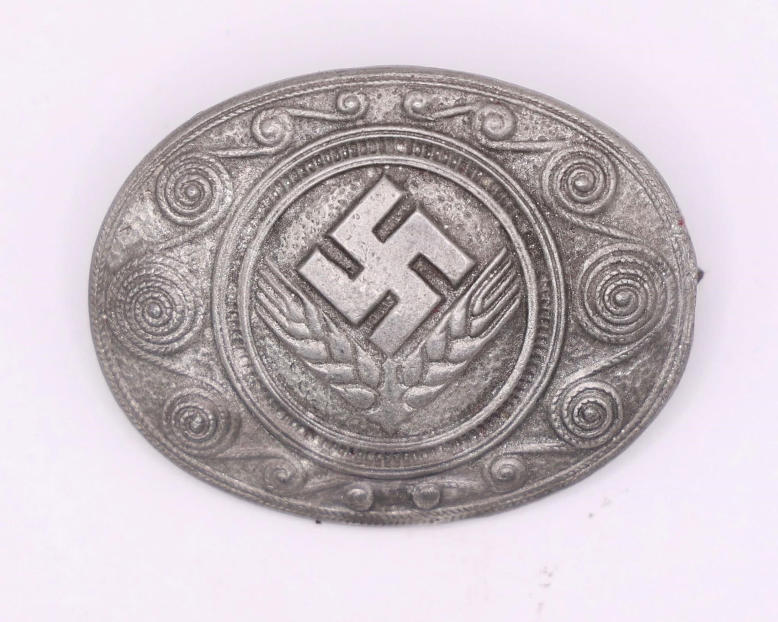 1930s German NSBO Tinnie Badge with Swastika: German NSBO (National Socialist Factory Cell Organization) tinnie badge from the 1930s. Metal pin featuring a central swastika above wheat ears with decorative scroll border. Issued as a