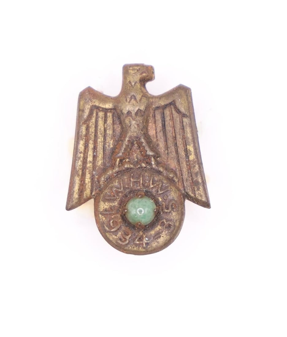 German WHW 1934-35 Badge: German Winterhilfswerk (WHW) 1934-35 hollow-backed alloy badge with bronze finish, depicting an eagle with down-swept wings clutching a circular plate inscribed "W.H.W. 1934-35" and set with a green g