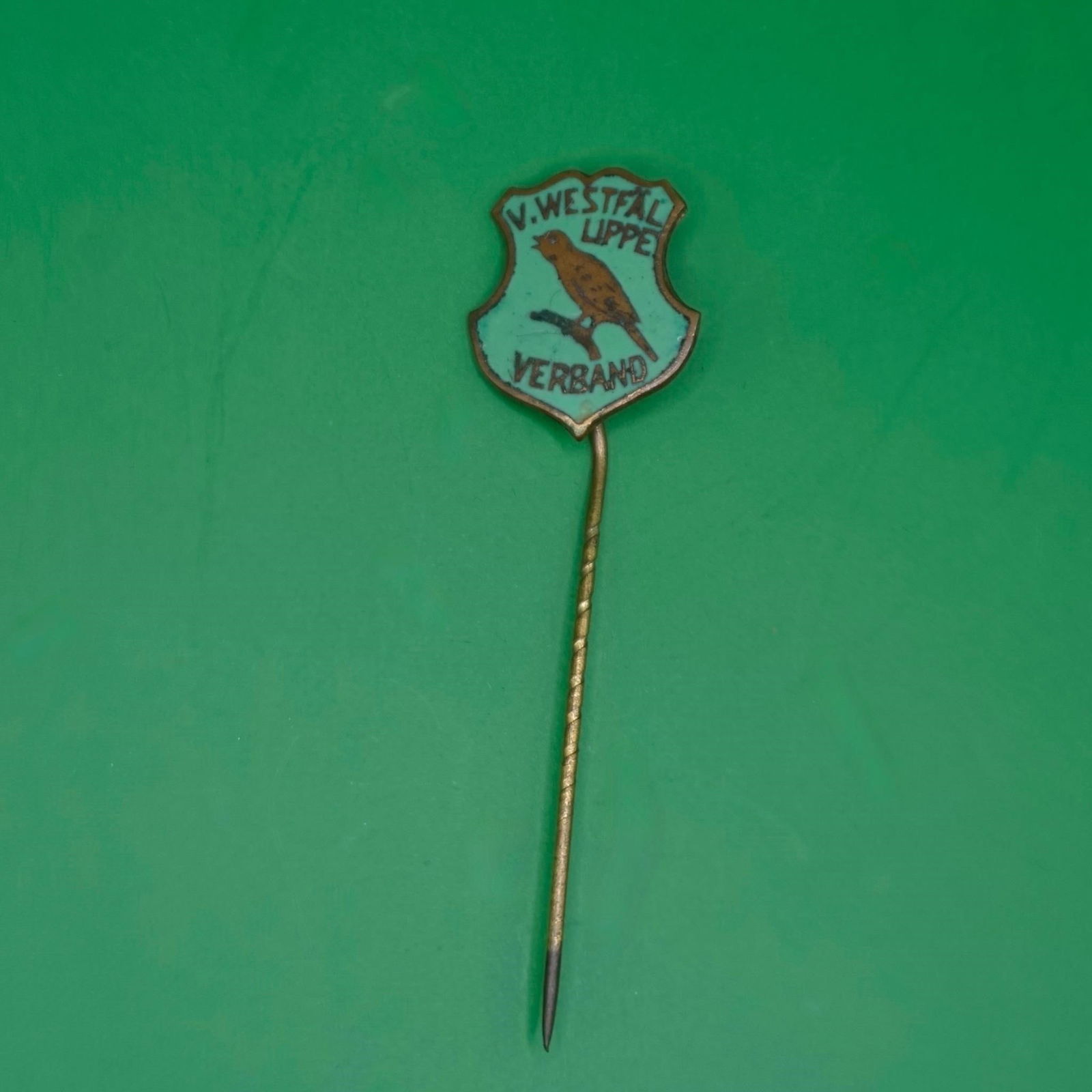 Vintage V. Westfal Lippe Verband Enamel Stick Pin: A small vintage enamel stick pin with a shield-shaped badge at the top. It has a light turquoise background, a brown bird perched on a branch in the center, and black text reading "V. WESTFAL LIPPE"