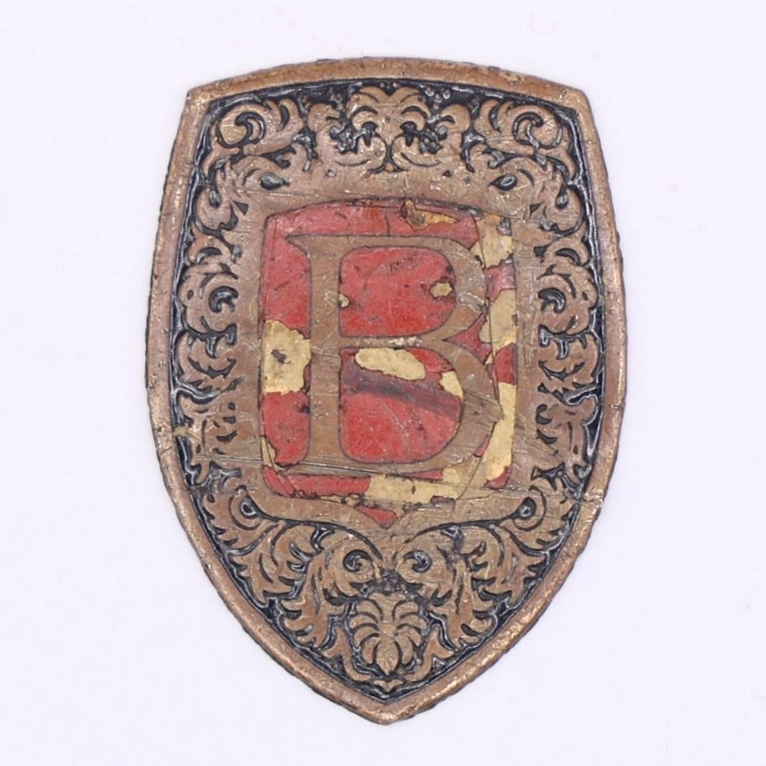 German Metal Shield Badge "B": This is a small metal shield badge with ornate scrollwork and a prominent red "B" at the center. The design suggests it was a decorative or uniform-style emblem, likely representing an organization, s