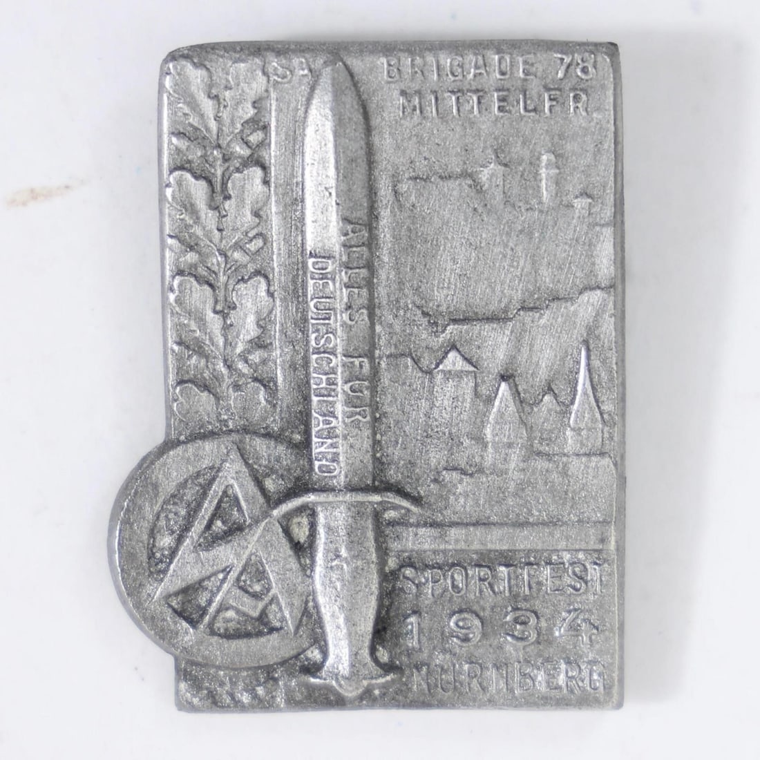 German SA Sportfest 1934 Nürnberg Tinnie Badge: This item is a German SA Sportfest 1934 Nürnberg "tinnie" badge, likely produced from stamped tombac or brass with a silvered finish.