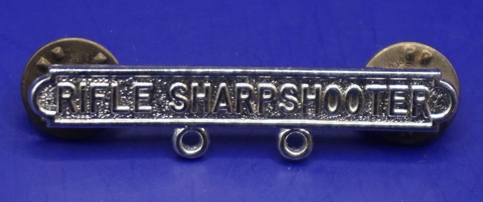 WWII Rifle Sharpshooter qualification Badge: This is a military marksmanship qualification badge for a Rifle Sharpshooter. It is awarded to military personnel who achieve a specific level of proficiency with a service rifle. The qualification