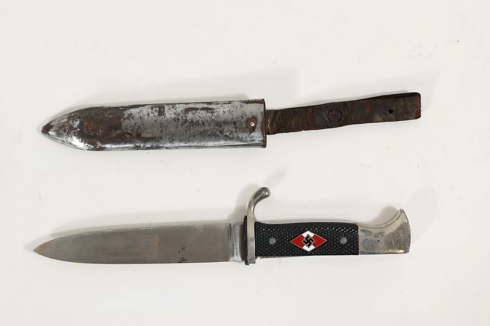 WWII German Hitler Youth Knife: German youth organization knife from the WWII era with black checkered grip and inset diamond emblem. Metal guard and single-edge blade showing age, wear, and surface marks consistent with use. The