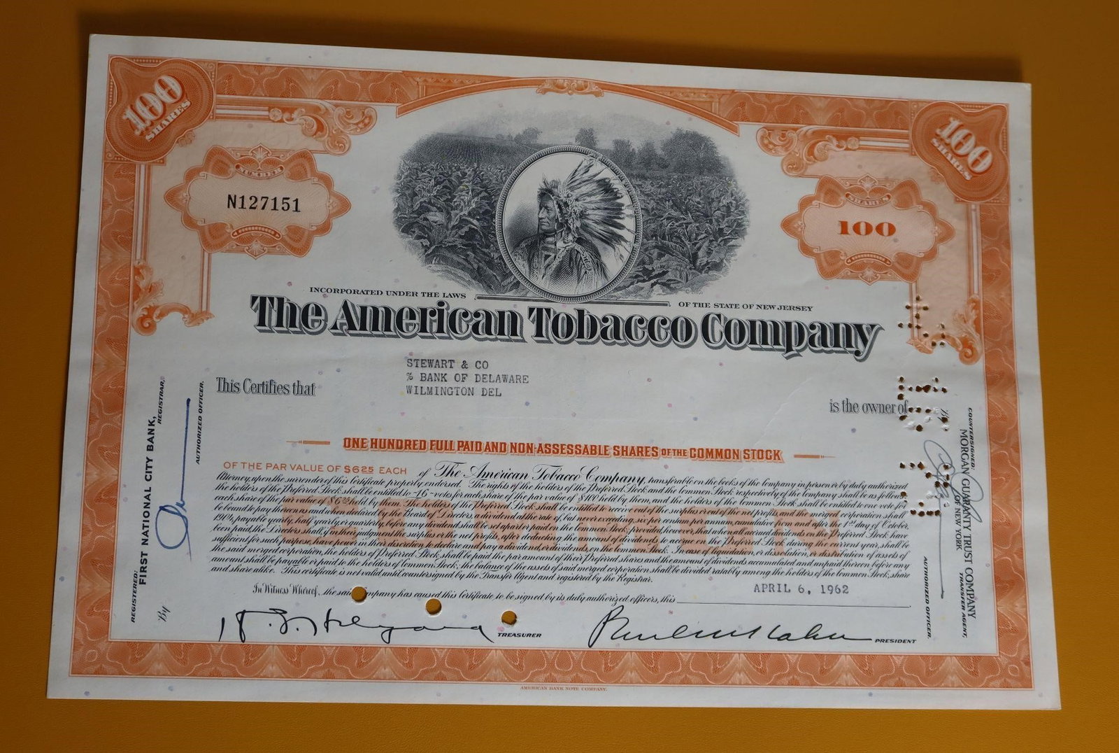 American Tobacco Company Stock Certificate: A vintage American Tobacco Company stock certificate issued on April 6, 1962. The certificate is for 100 shares of common stock. It features a vignette of an American Indian chief, often identified as