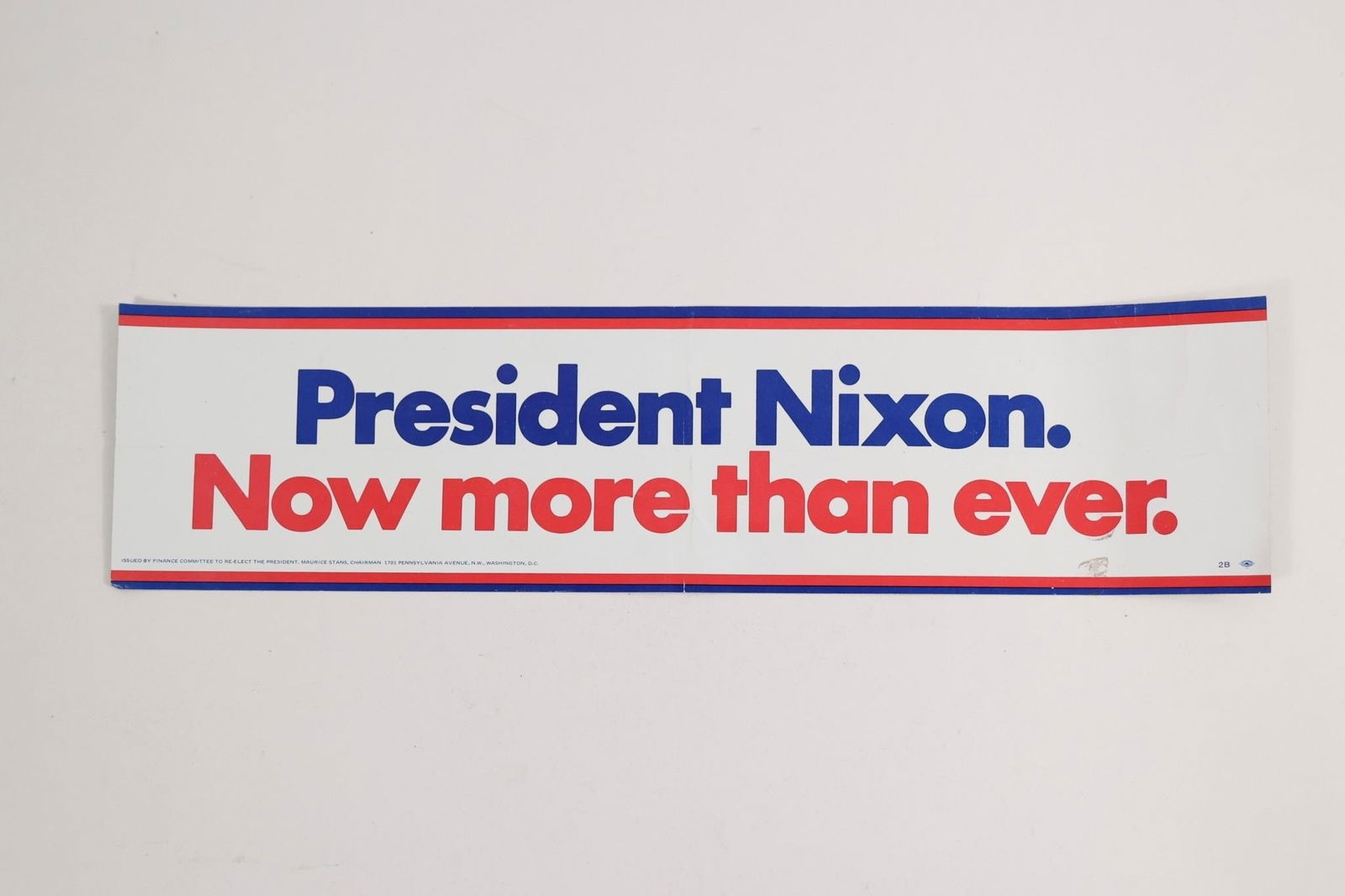 President Nixon Bumper Sticker: Long rectangular sticker reading "President Nixon. Now more than ever." in blue and red lettering with red and blue border lines. Small printed line at bottom reads "Issued by Finance Committee to